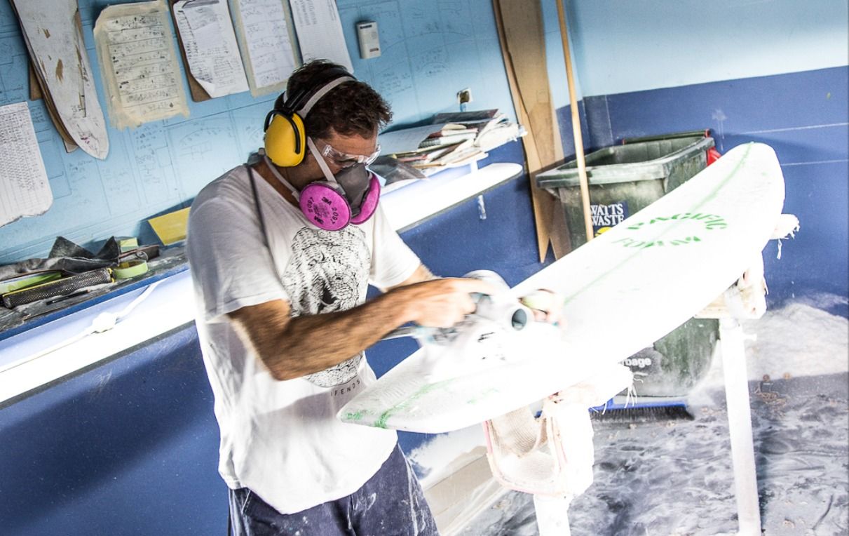 Person spray painting a large surface with white paint using professional equipment in an industrial setting.