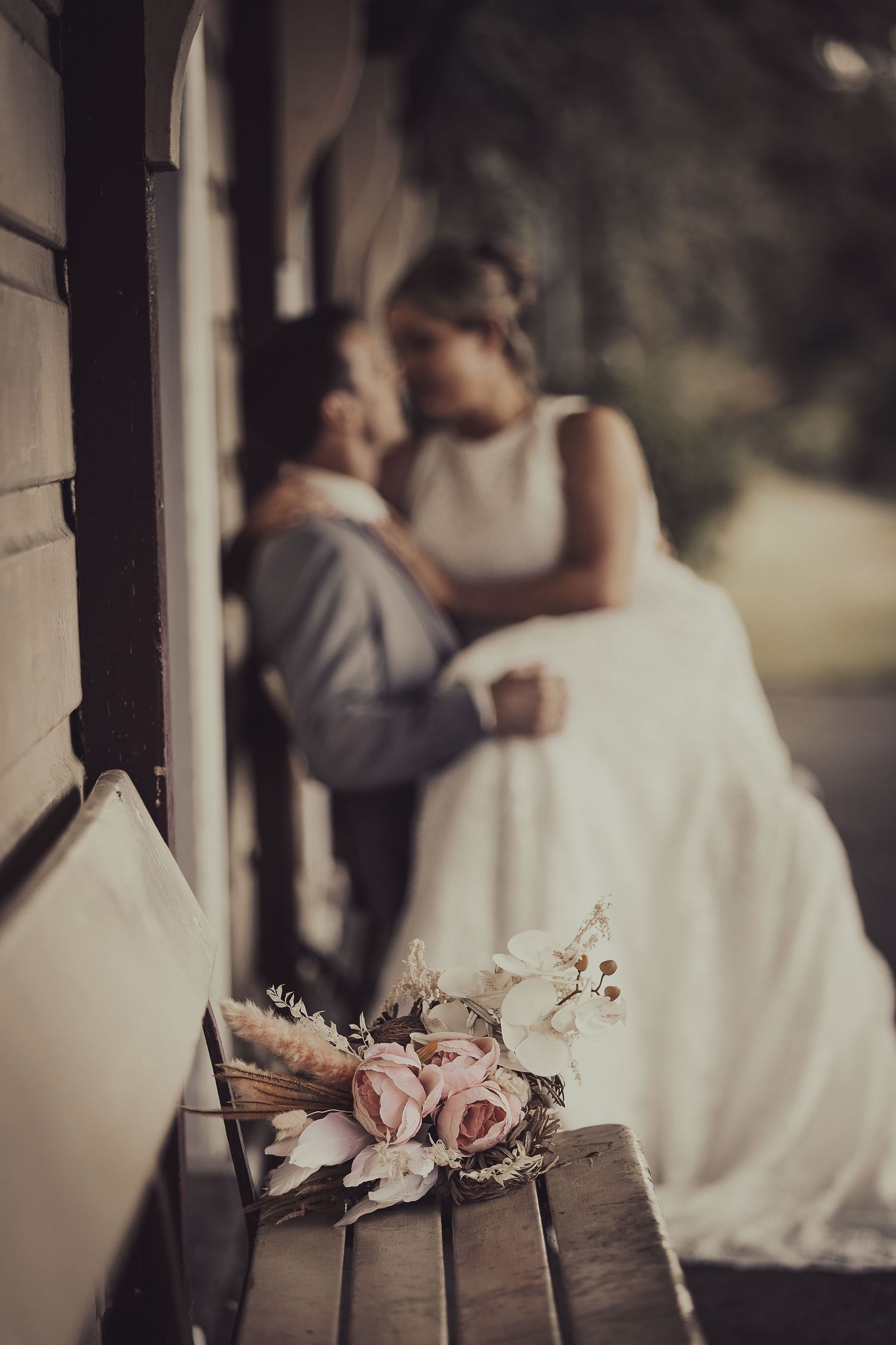 Romantic vintage-style wedding photo with a delicate pink rose bouquet on a rustic wooden bench in soft lighting.