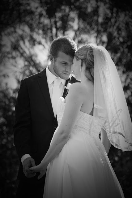 Black and white wedding photo showing a tender moment between a bride in a flowing gown and groom in a classic suit.
