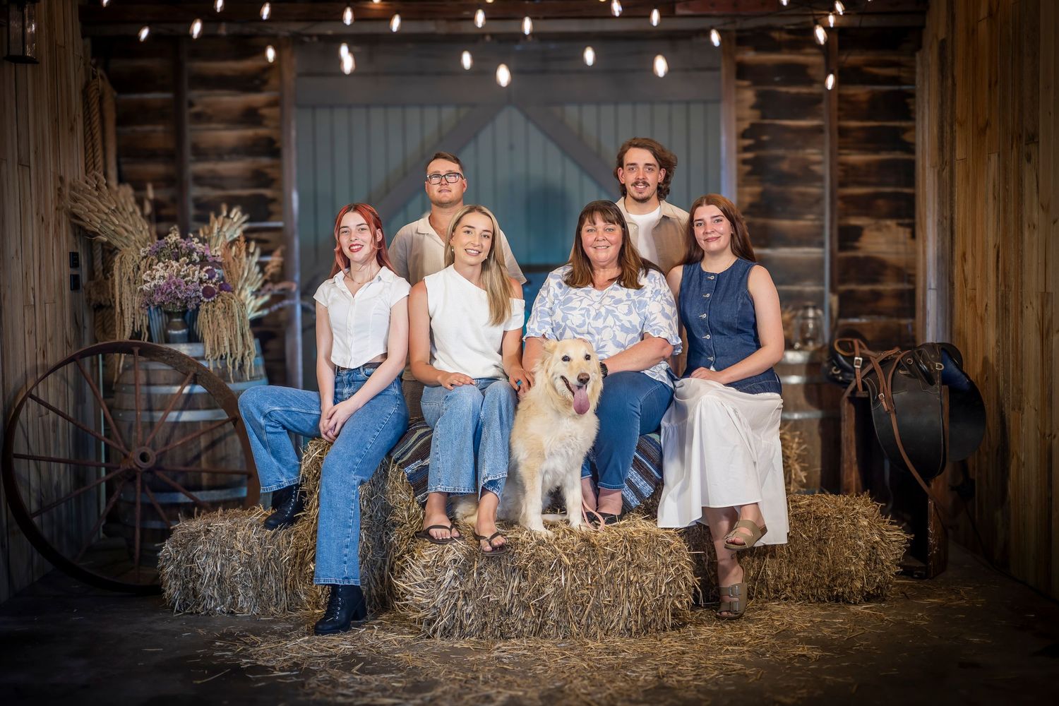 A rustic family portrait session featuring multiple poses on hay bales inside a wooden barn.