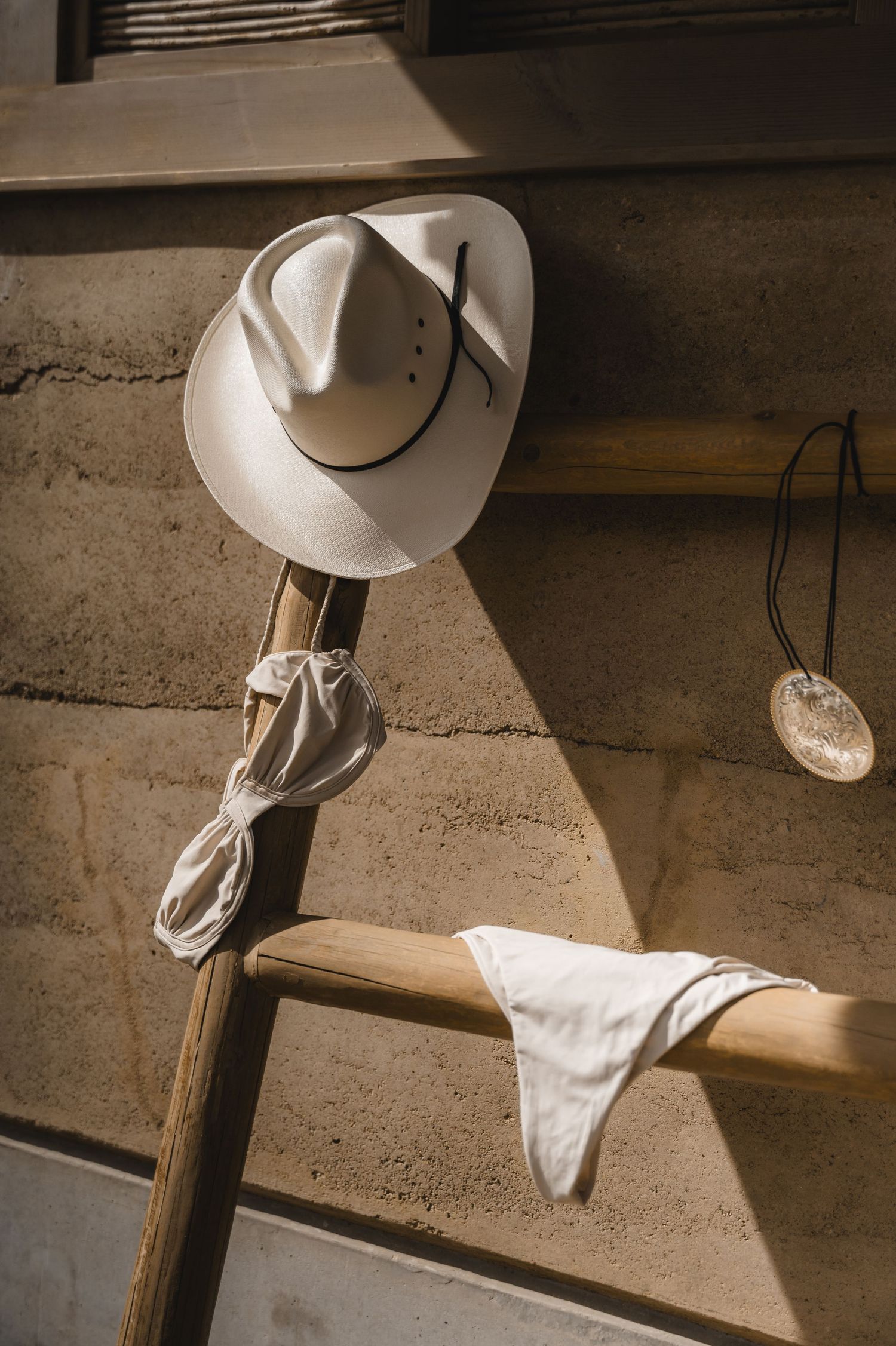White cowboy hat hanging on a wooden post in dramatic lighting.