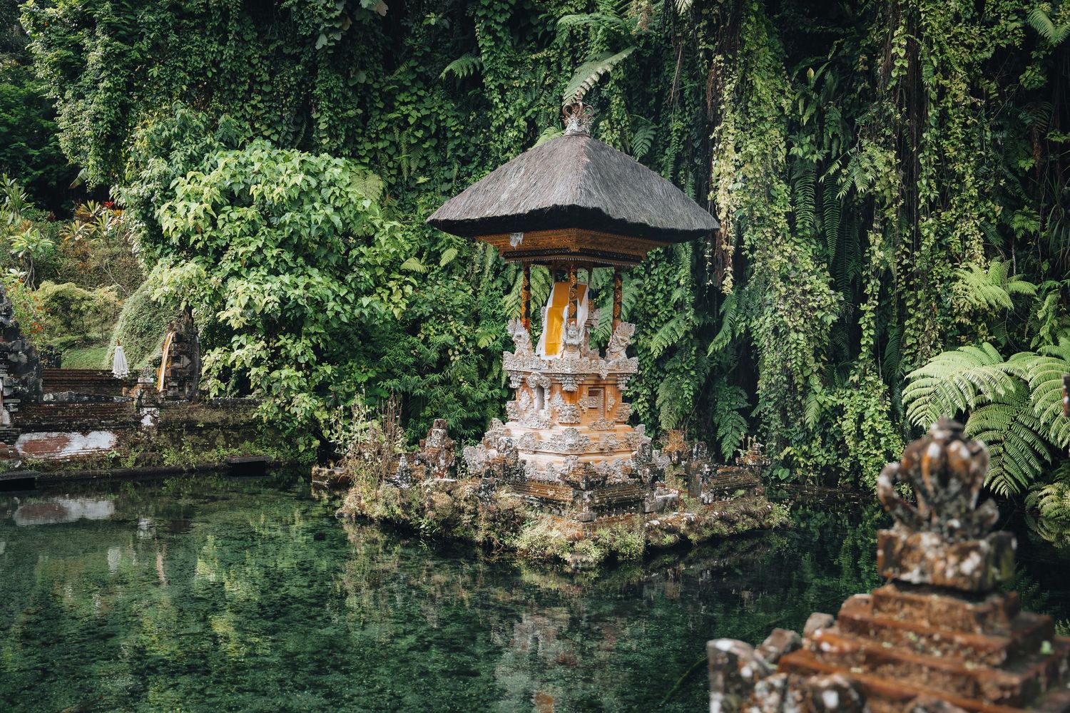 Traditional Balinese temple structures nestled among lush tropical vegetation and stone walls.