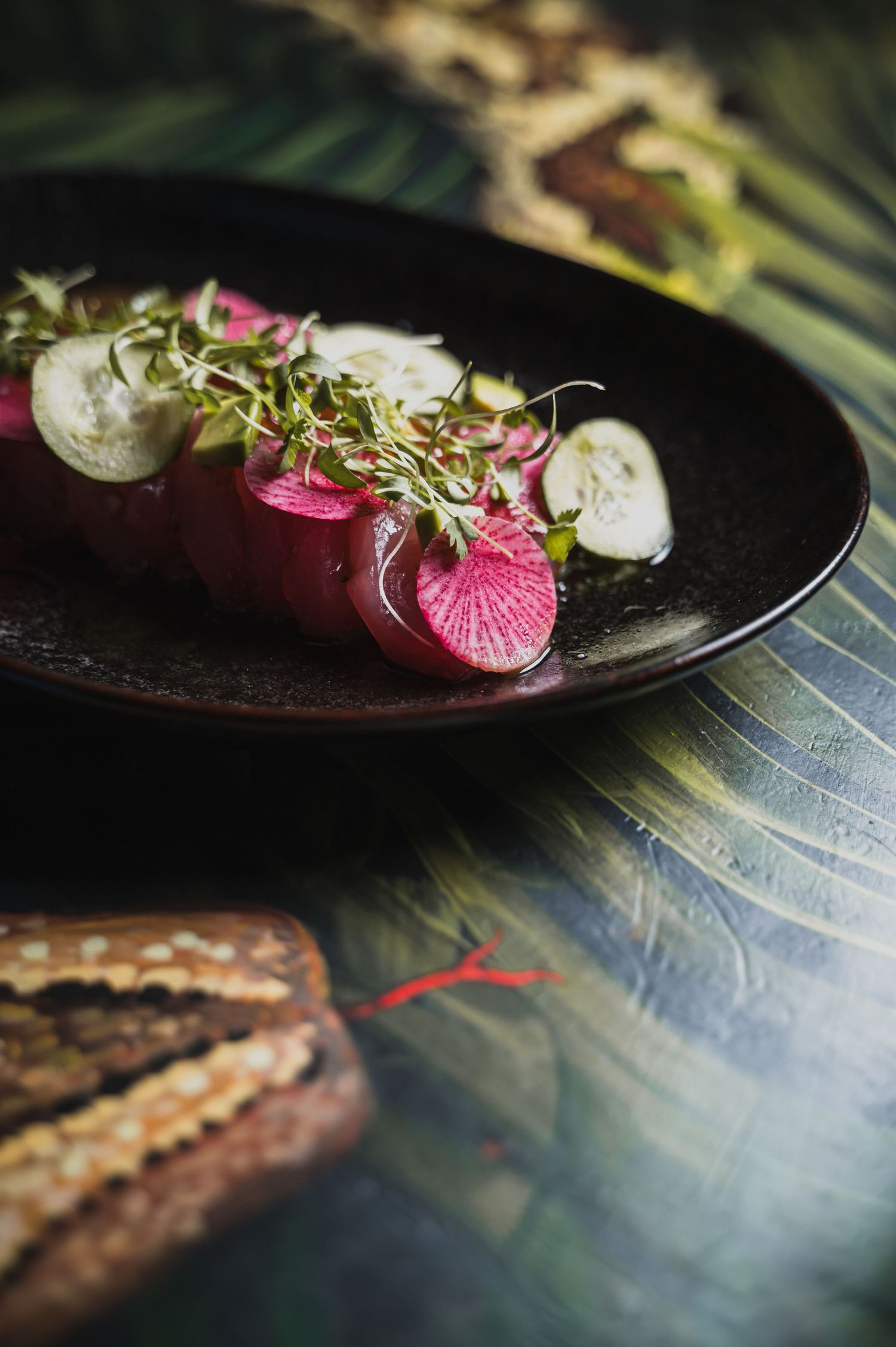 Sliced radishes and microgreens artfully plated on black ceramic dish.