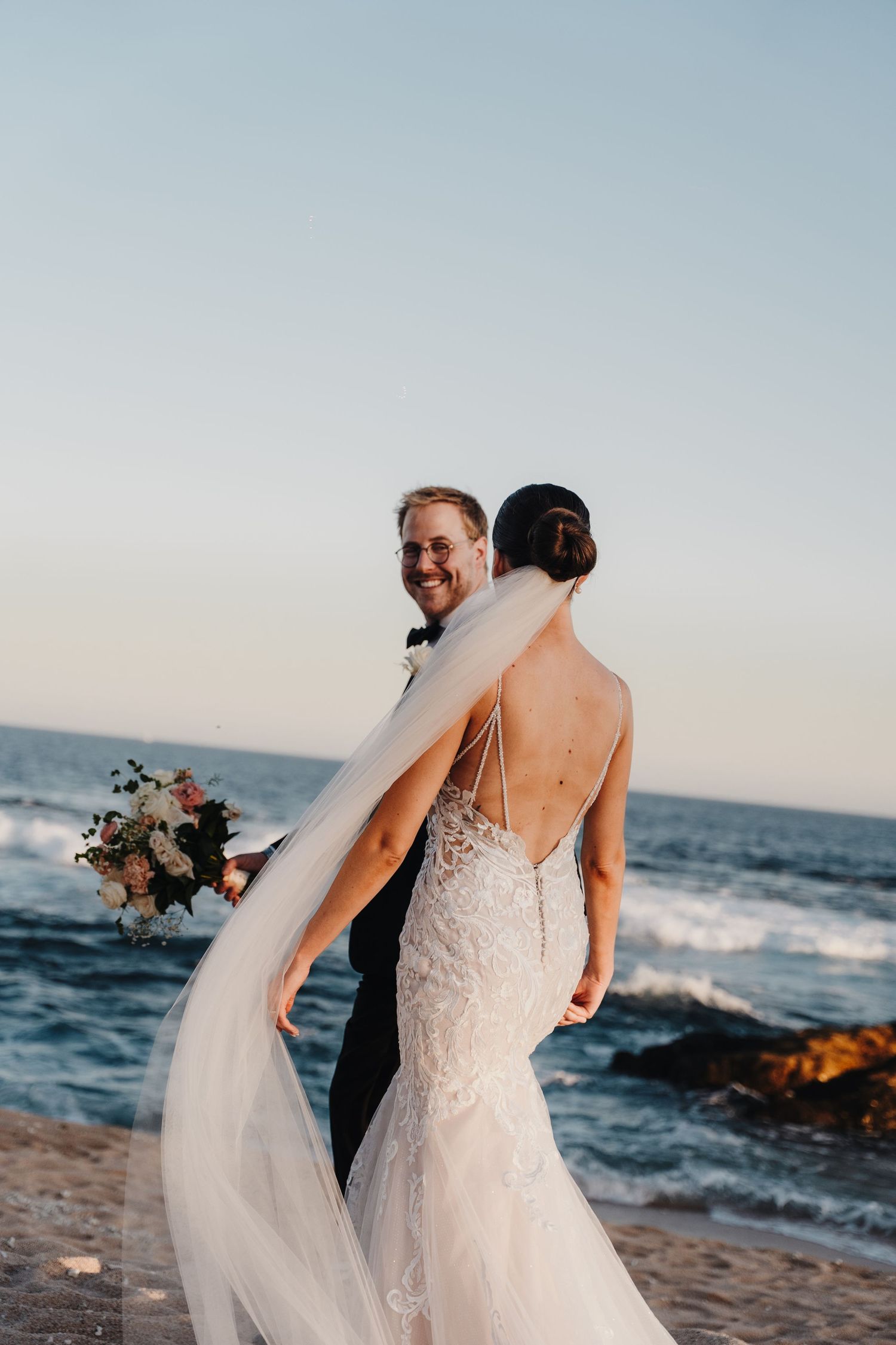 A joyful oceanside wedding moment captured with flowing veil and bouquet against the sea.
