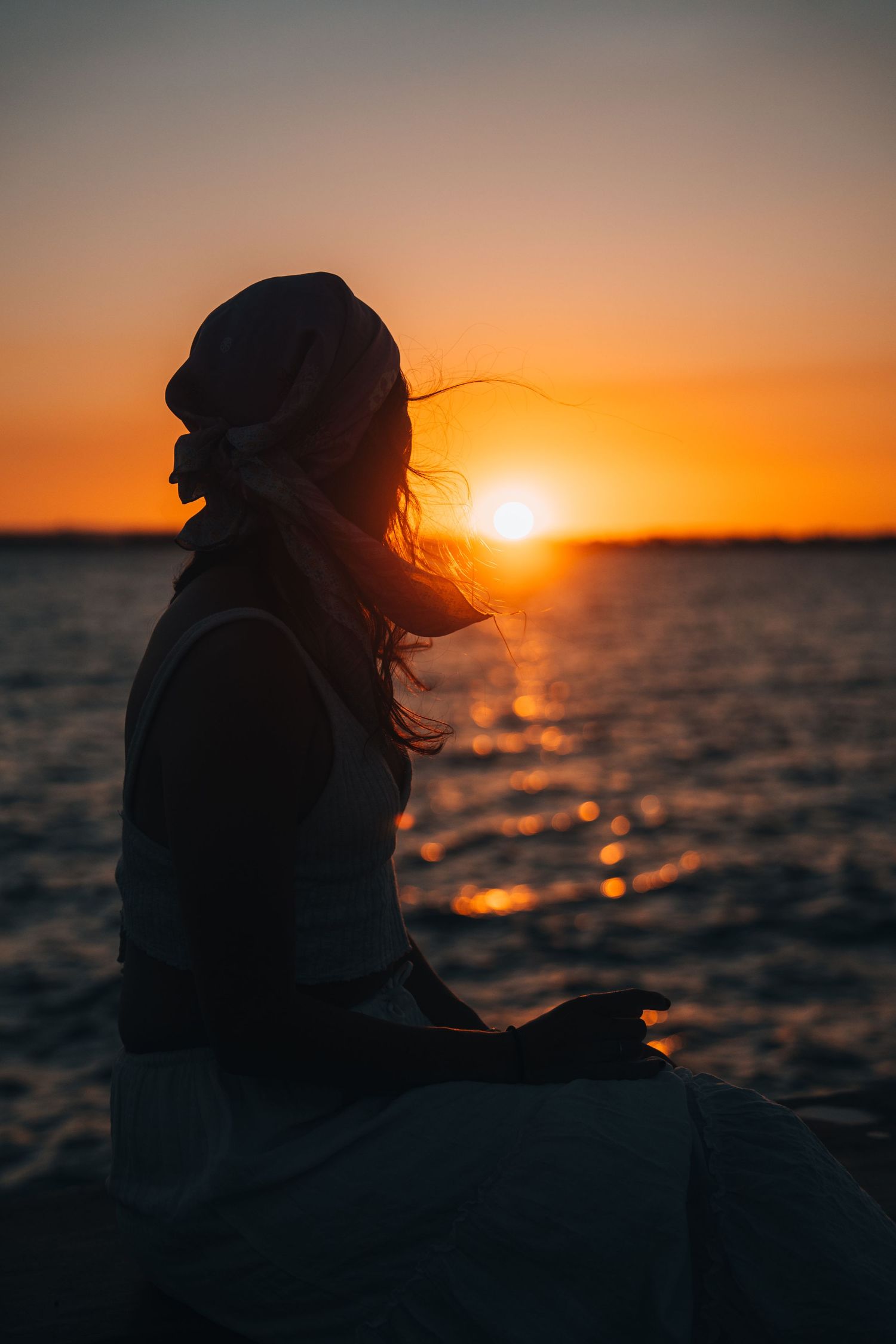 Silhouette at sunset overlooking calm ocean waters during golden hour.