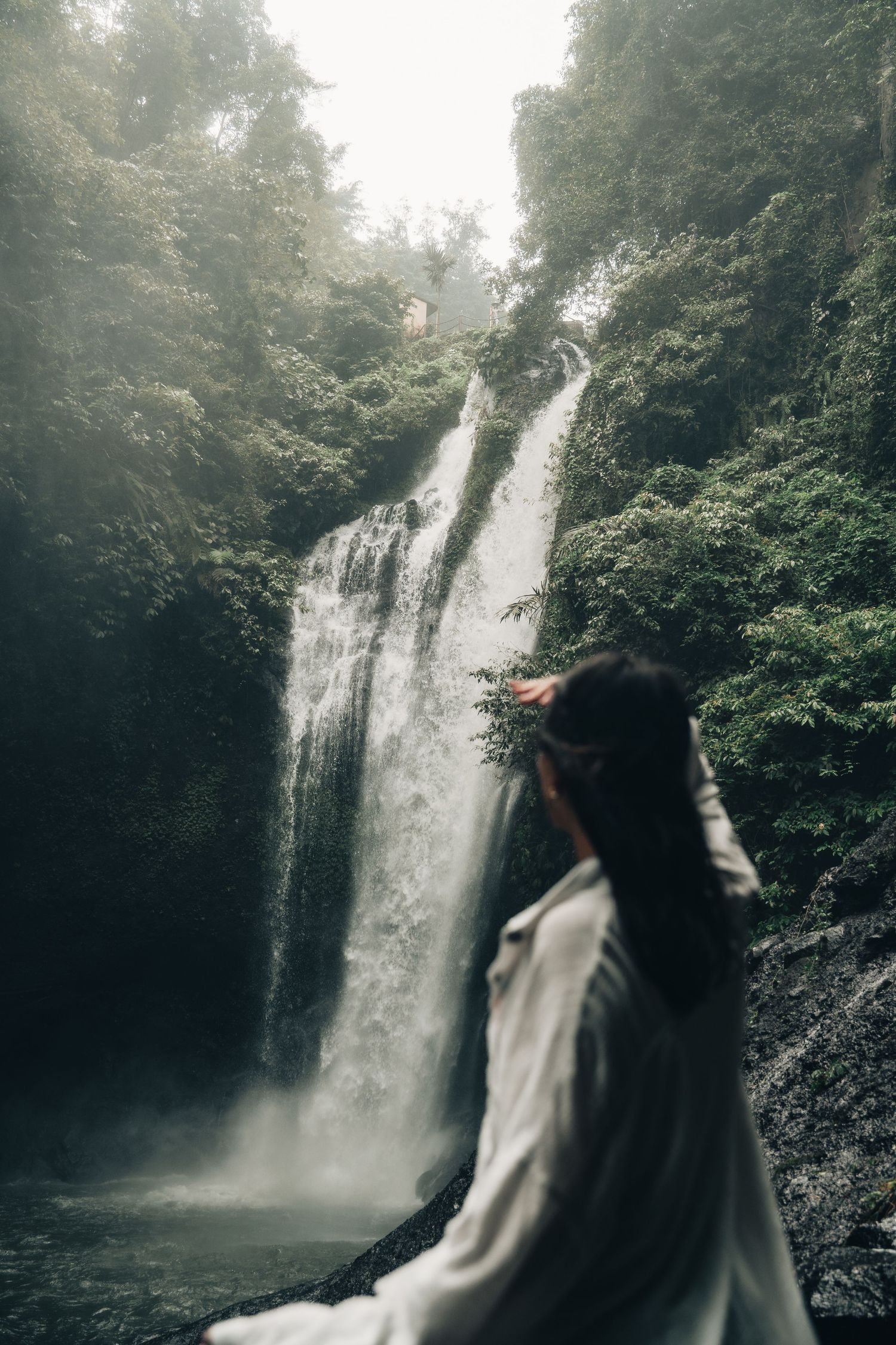 Majestic double waterfall viewed through misty forest with viewer in foreground.