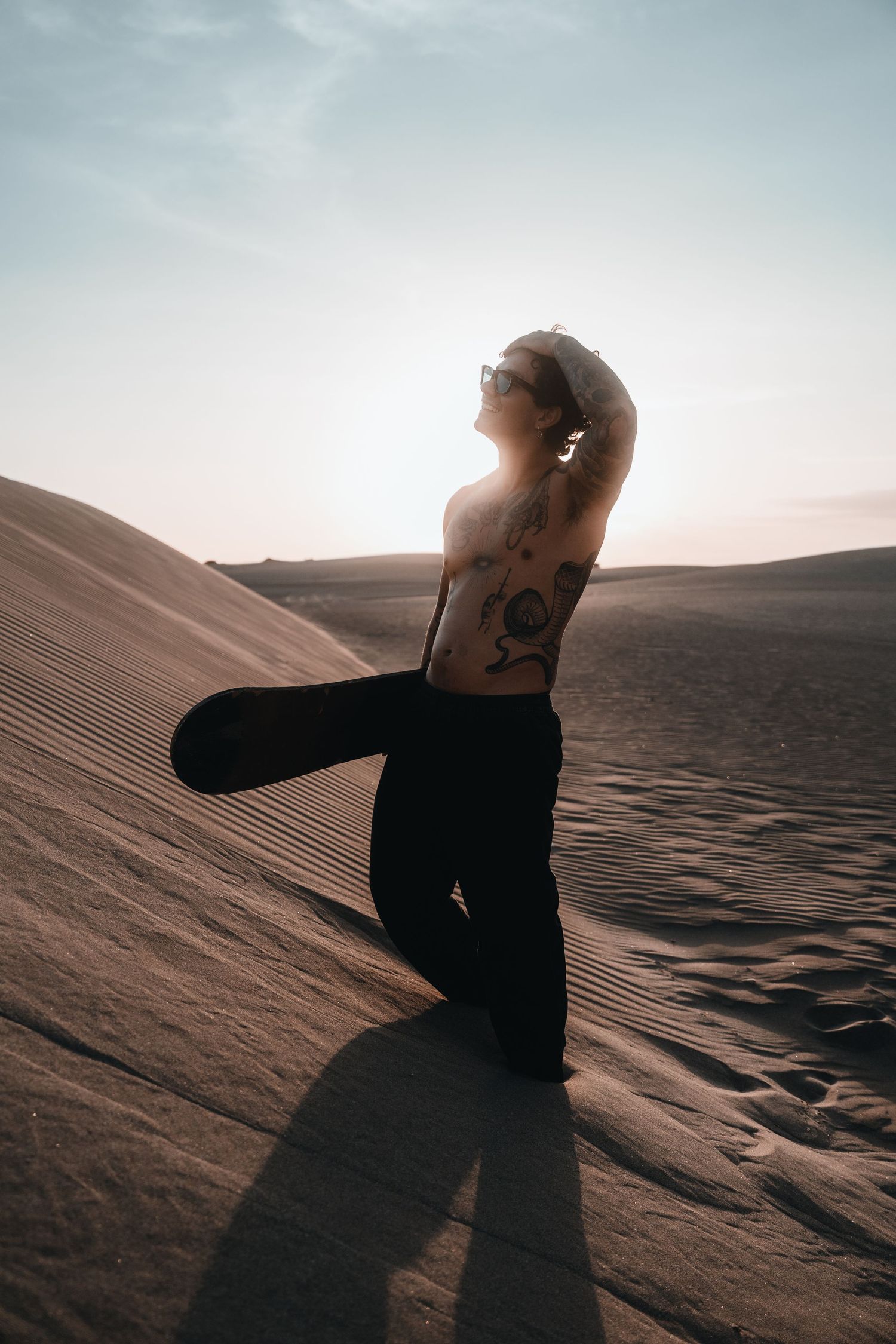 Person in black clothing sitting on desert sand dune during golden hour with dramatic shadows.