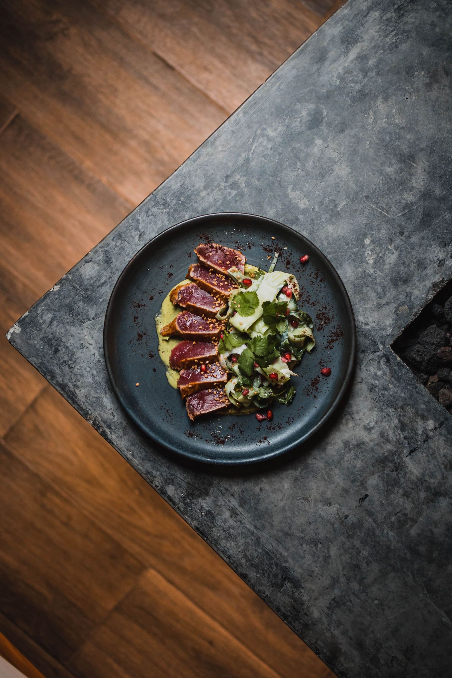 Seared tuna slices with micro greens plated on dark ceramic dish.