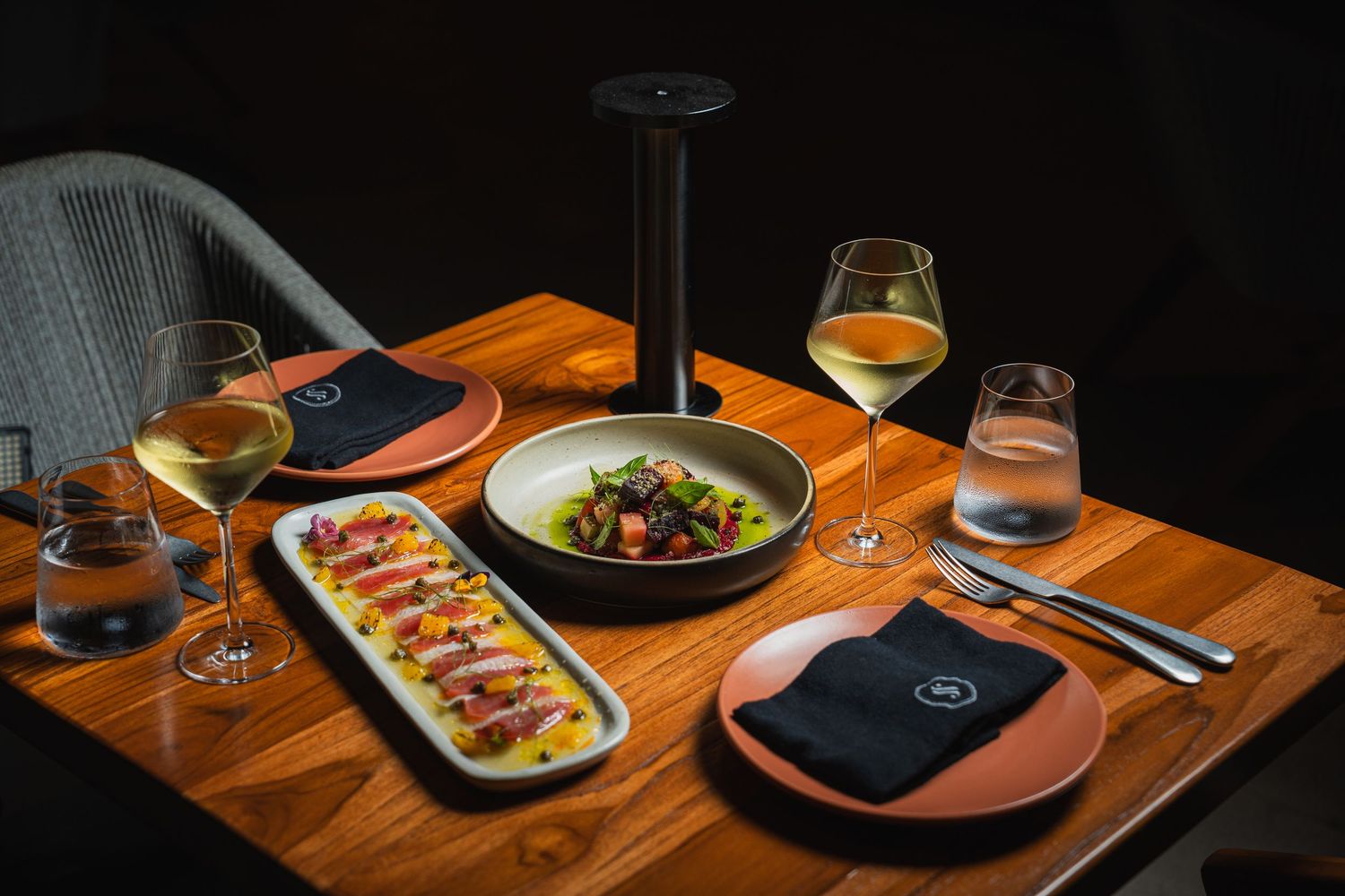 Elegant table setting in dimly lit restaurant with wooden surfaces and plated dishes.