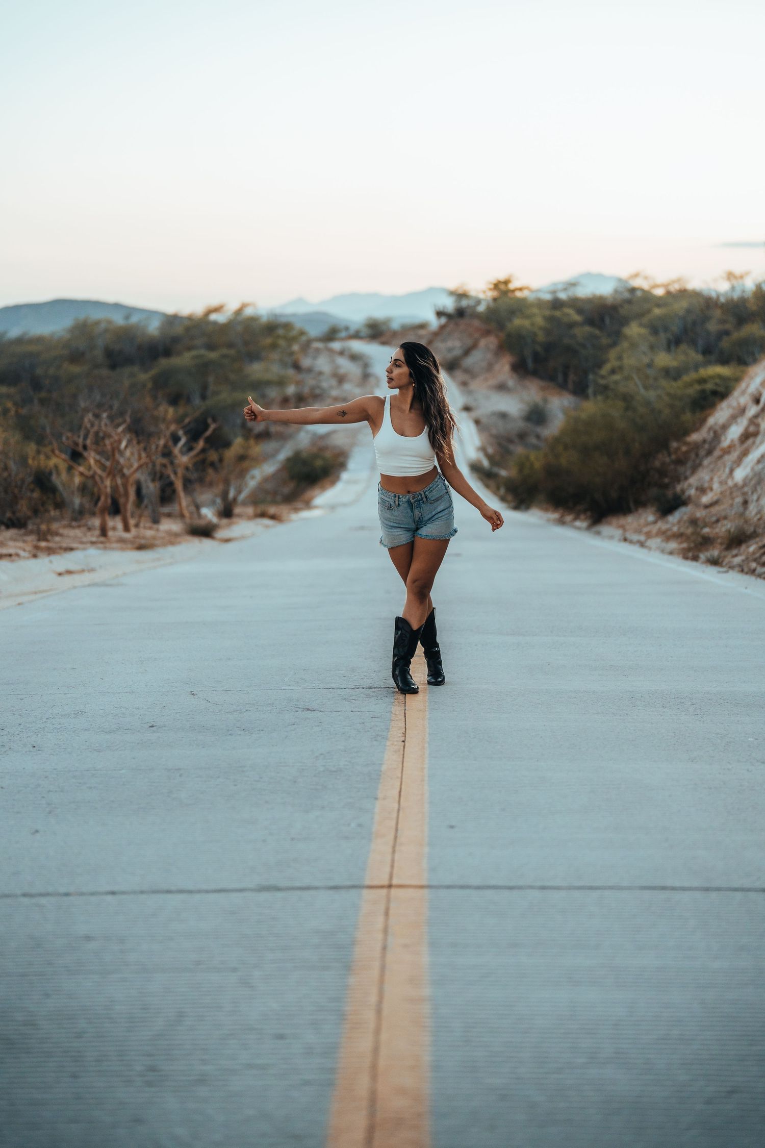 Person in casual wear walking along an empty desert road during daytime.