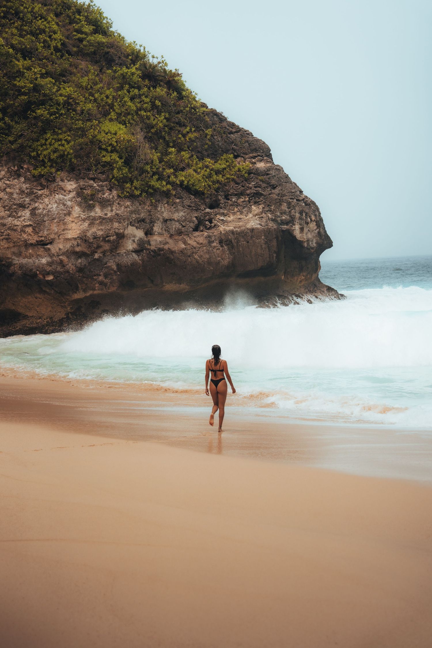 Person walking along a secluded beach with dramatic cliffs and turquoise waves.