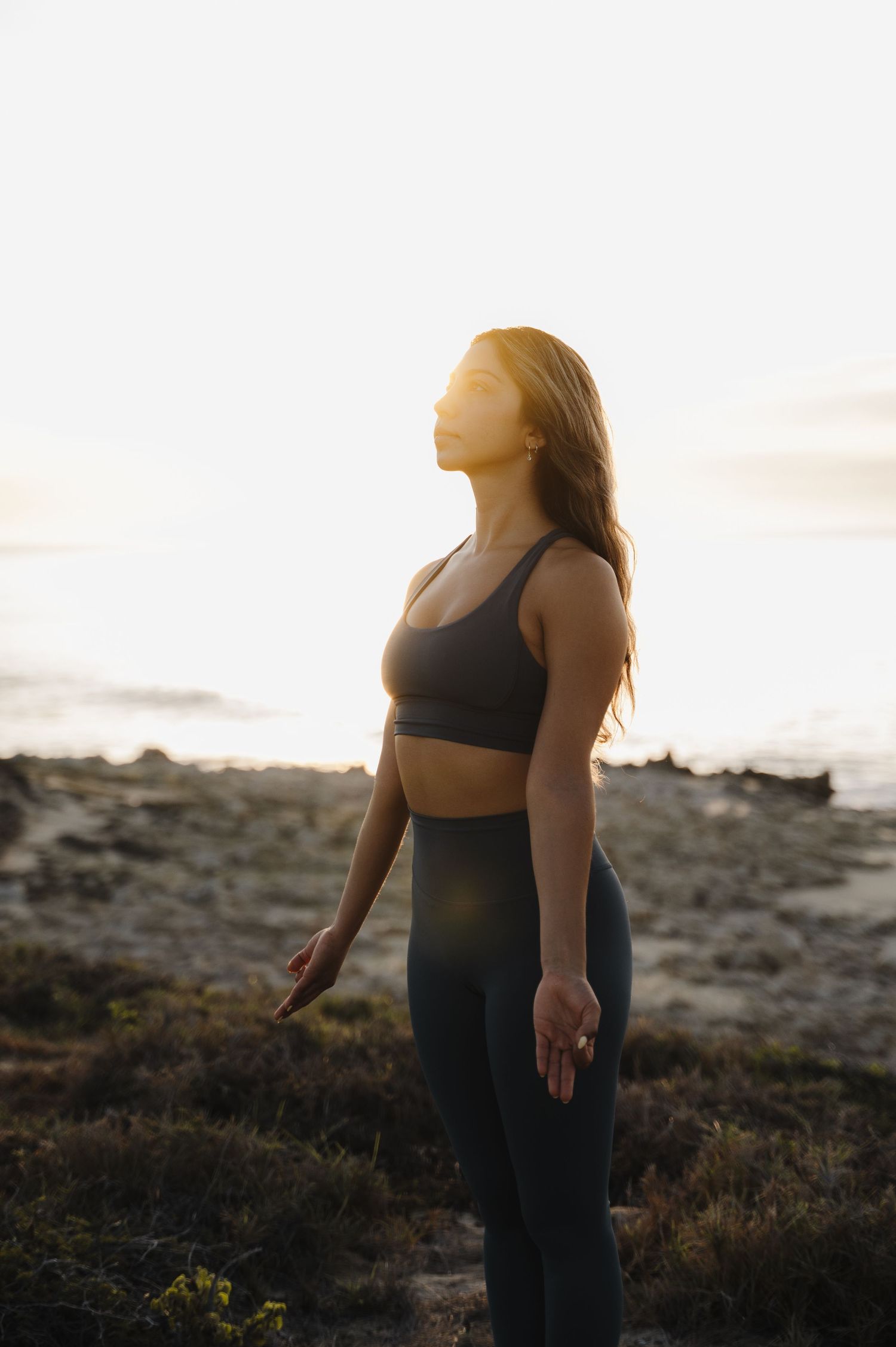 Silhouette figure in athletic wear stands against bright coastal horizon at sunset.
