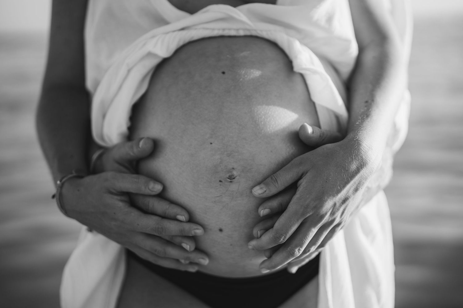 Close-up shots of loving hands cradling a pregnant belly in black and white.