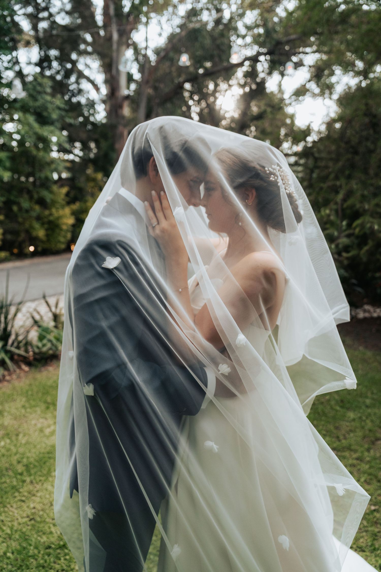 Romantic outdoor wedding moment captured through flowing white veil in garden setting.