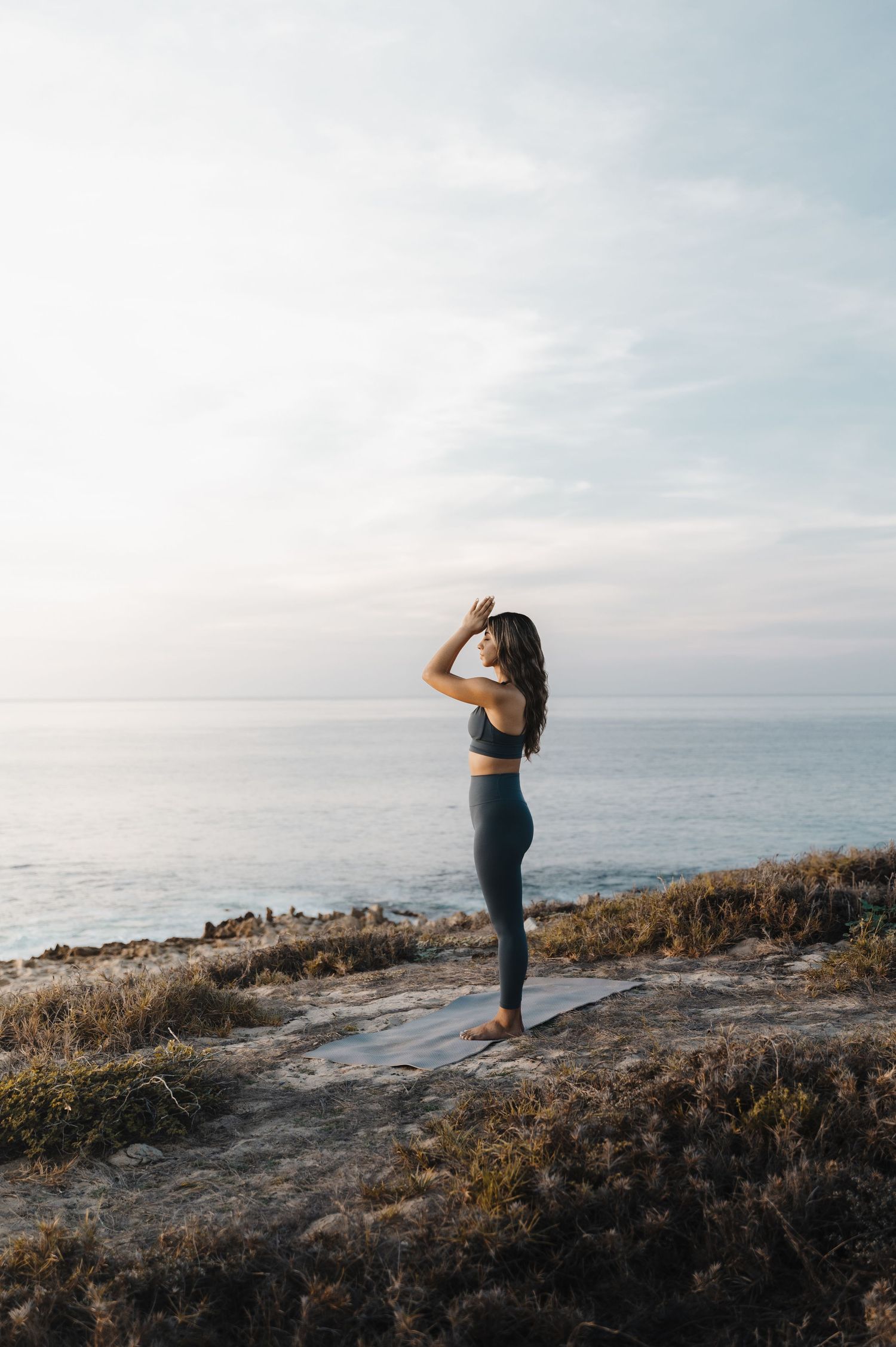 Athletic figure stretching on coastal cliffs overlooking ocean at sunrise.