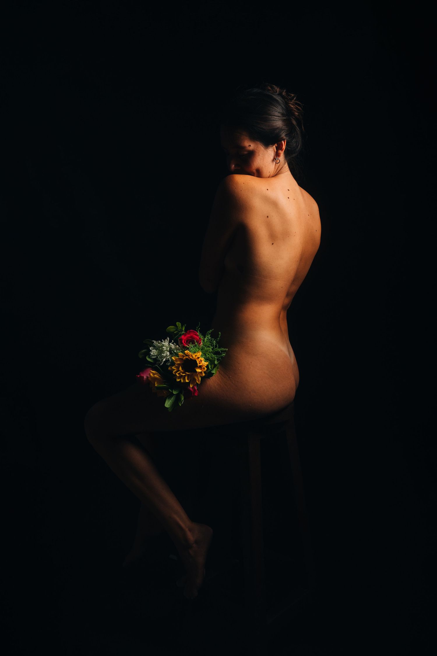 Artistic nude study with dramatic lighting and floral elements.