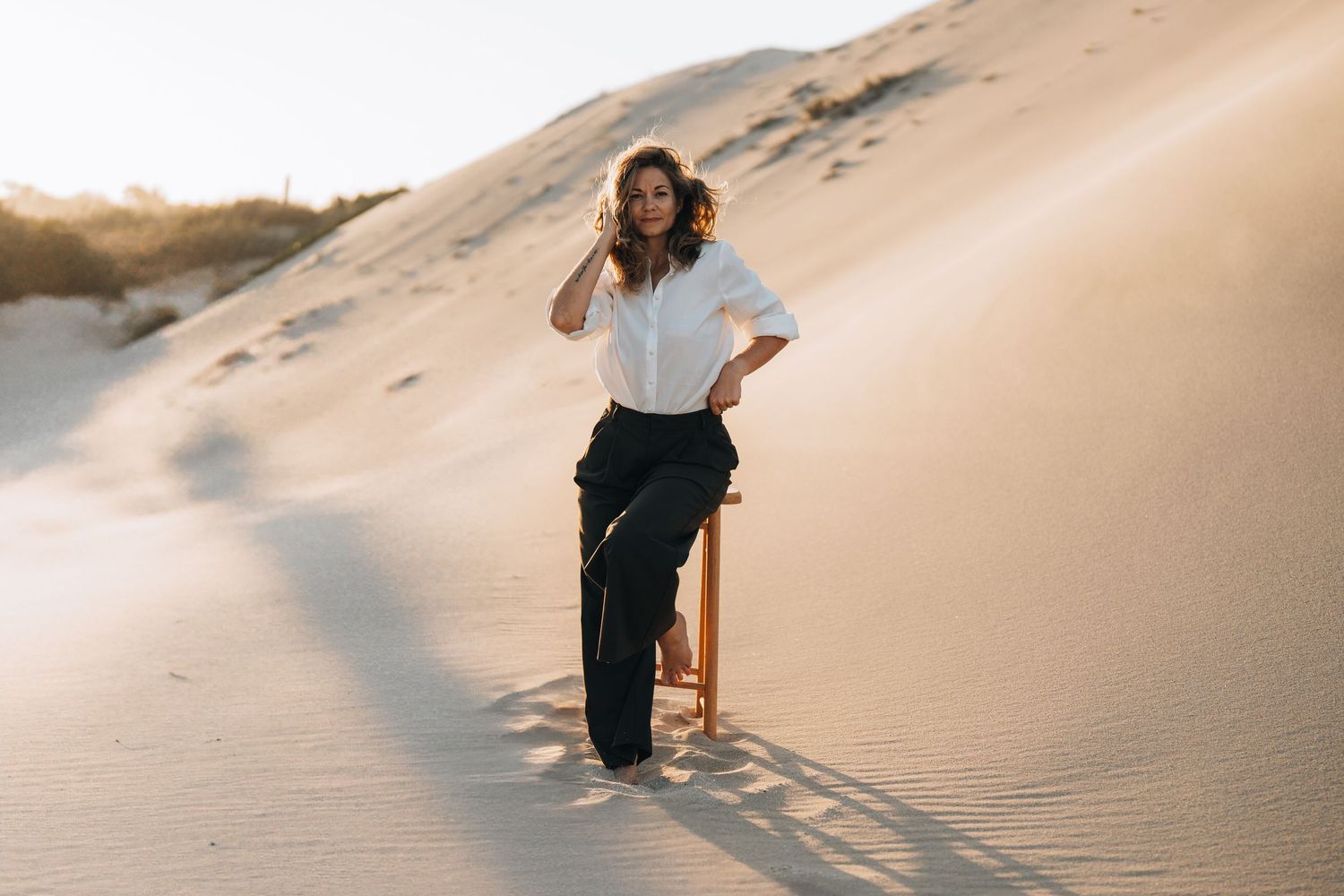 A romantic beach photoshoot with a flowing white dress against sandy dunes at sunset.