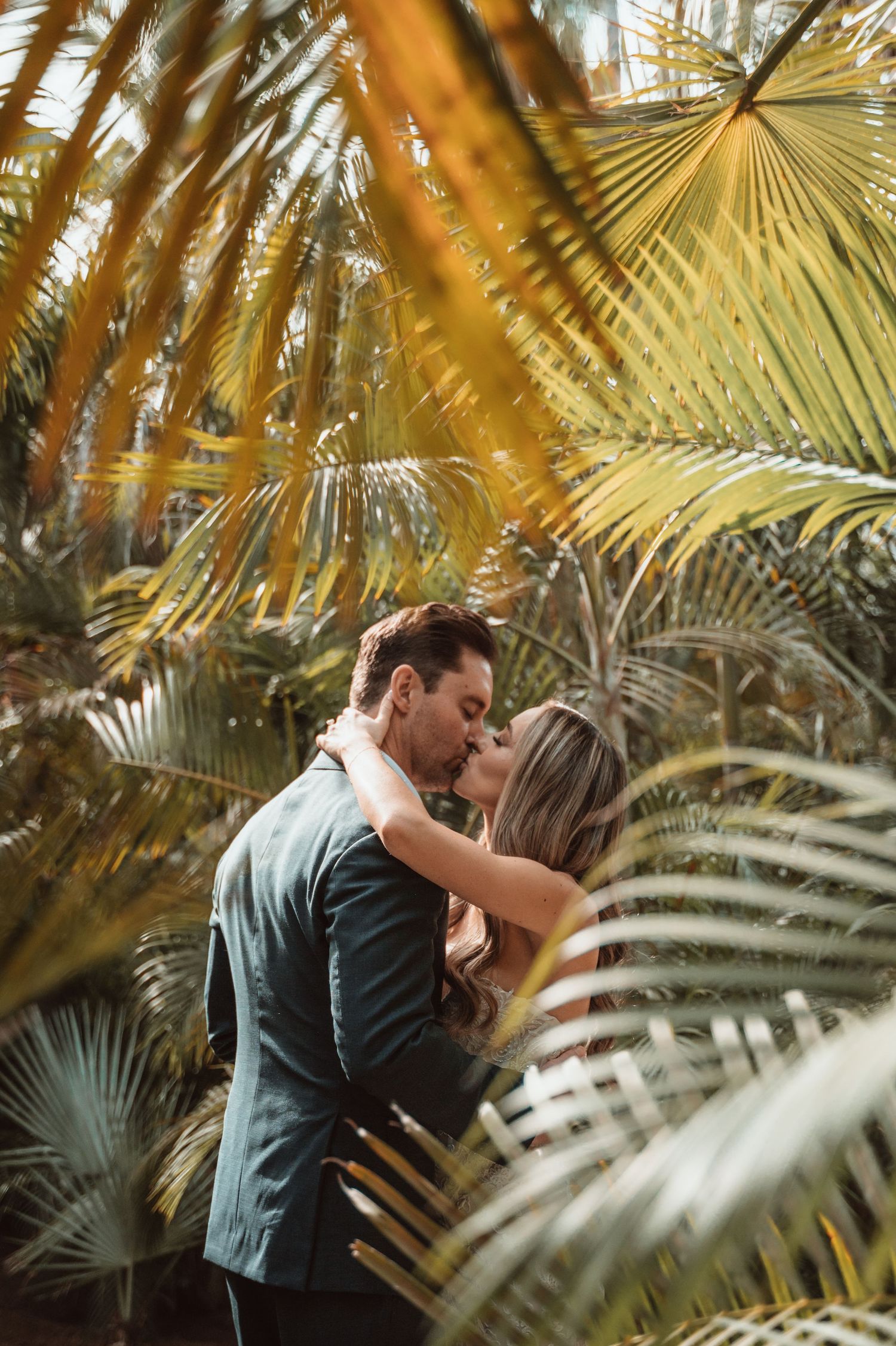 Romantic moment captured through golden palm fronds in tropical setting.