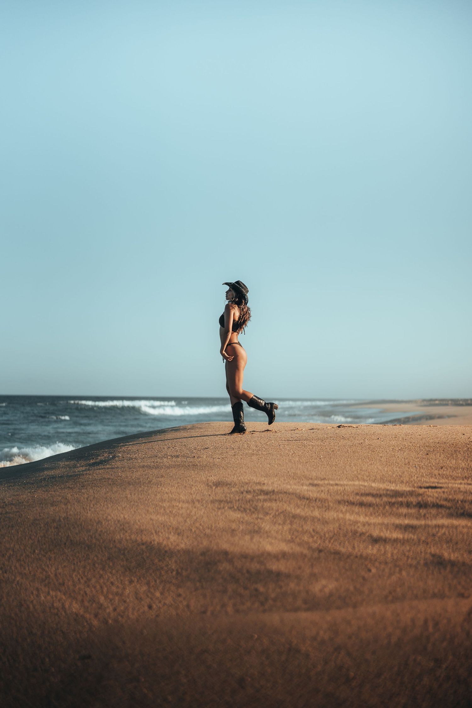 Minimalist beach scene with lone figure standing against ocean horizon on sandy shore.