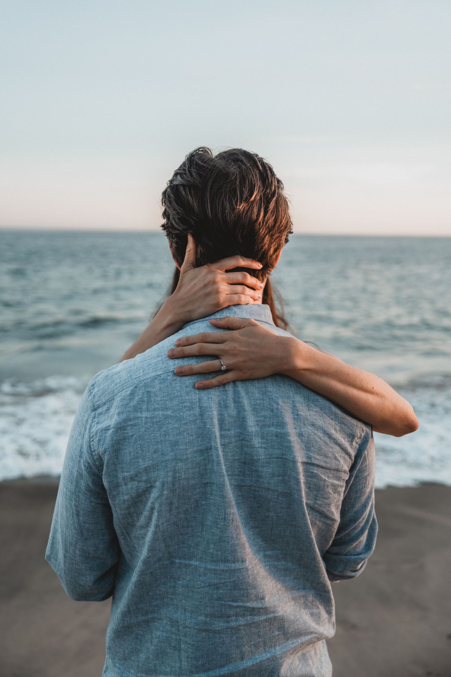 Person in a blue shirt looking out at the ocean waves during sunset.