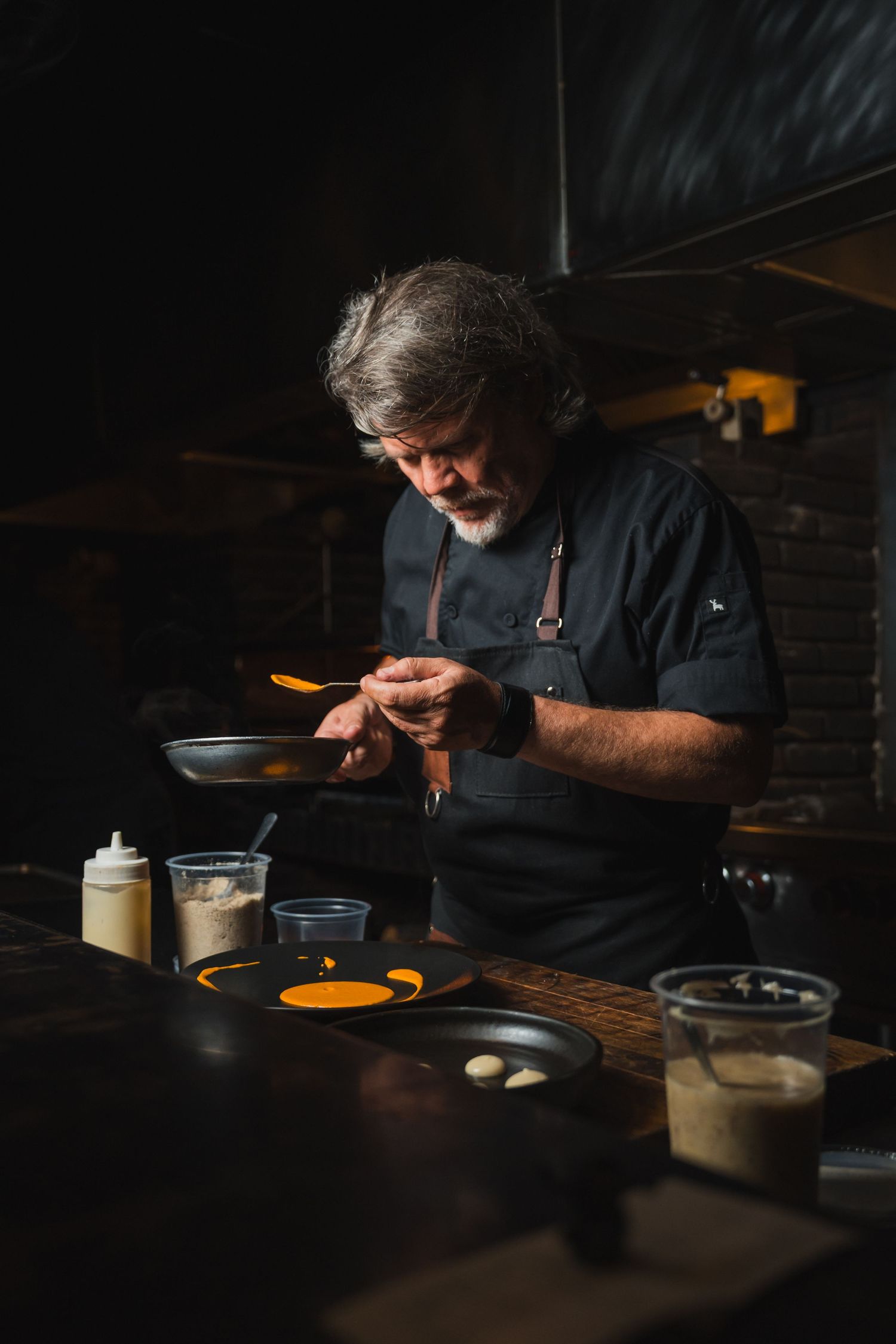 Chef preparing food in dark atmospheric lighting at a restaurant counter.
