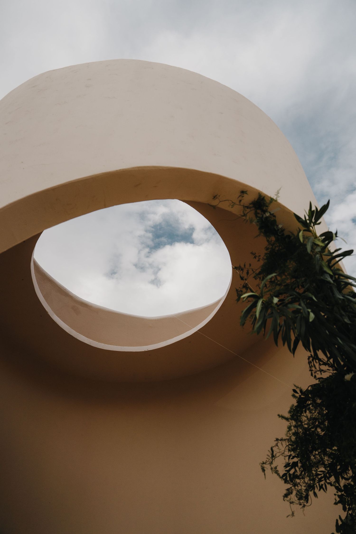 Modern architectural detail of curved white archway against cloudy sky.