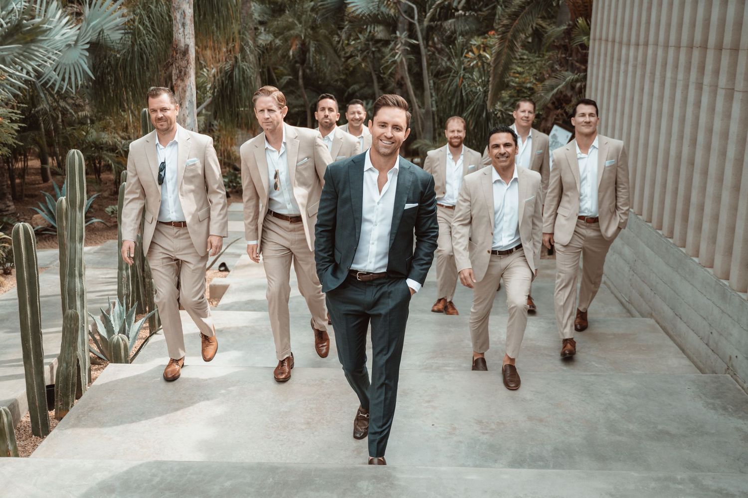 Wedding party walking in neutral tones along a concrete path.