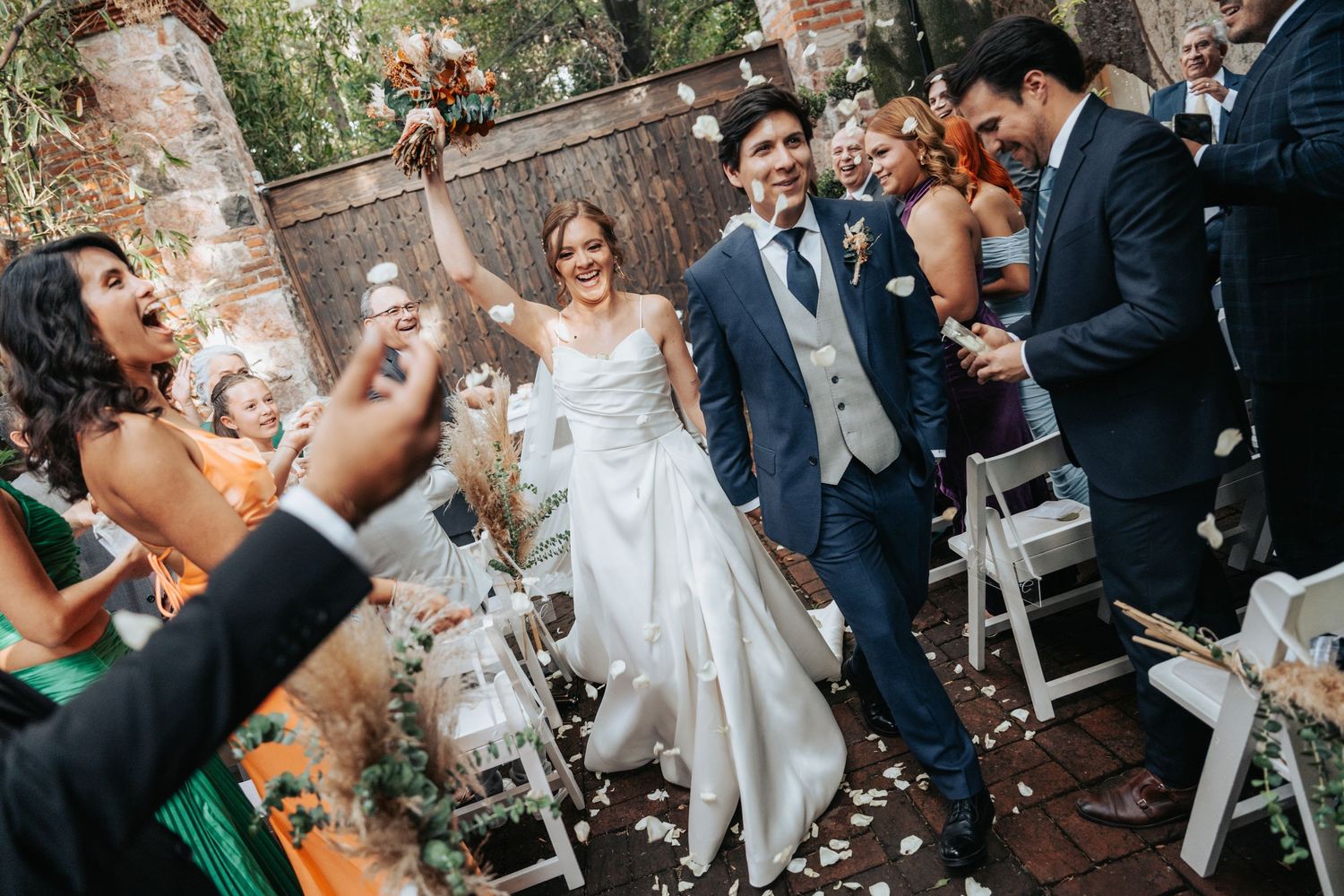 Wedding celebration scene with guests throwing confetti in an outdoor garden setting.