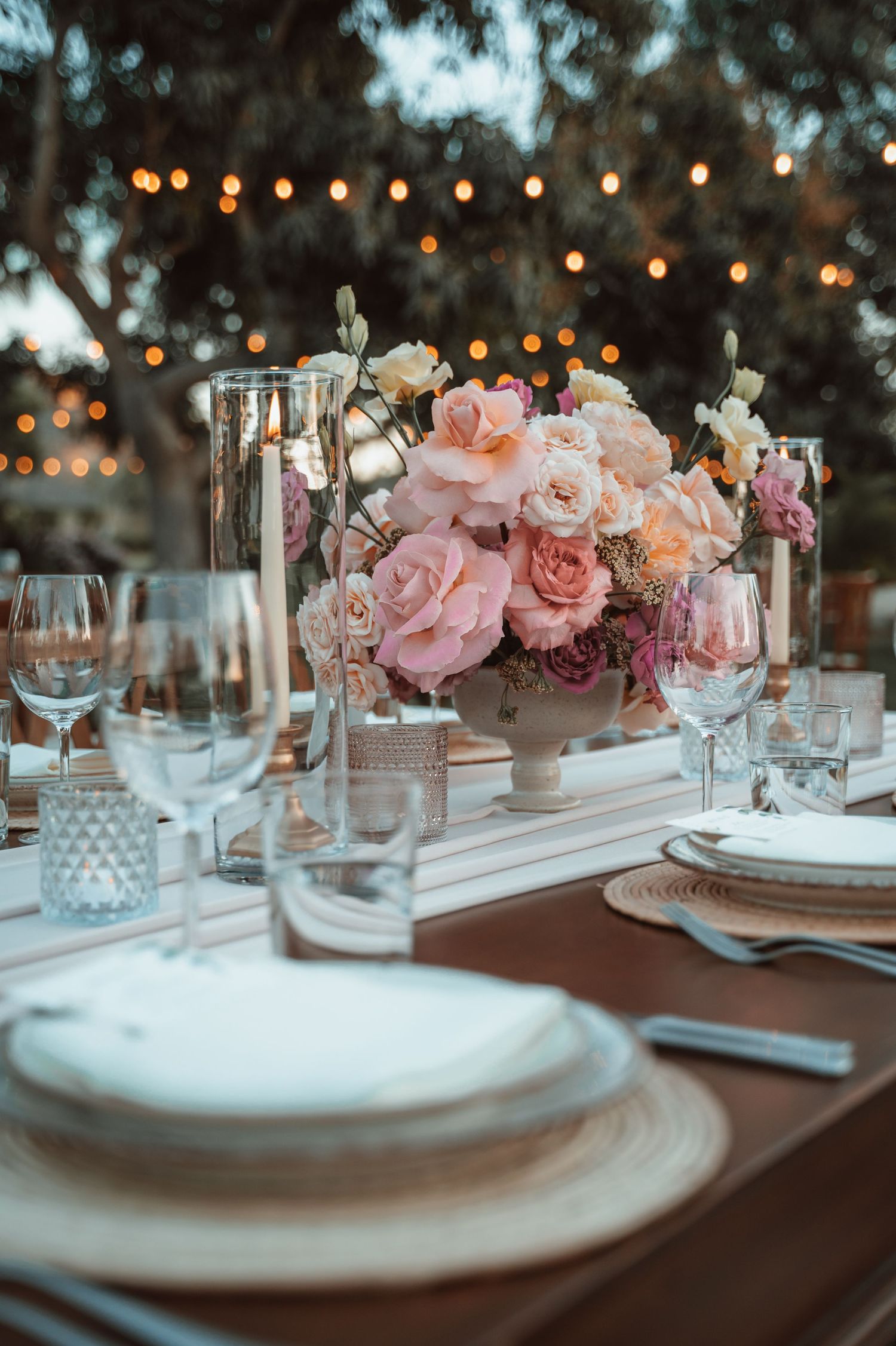 Elegant table setting with pink floral centerpieces and string lights for a wedding reception.