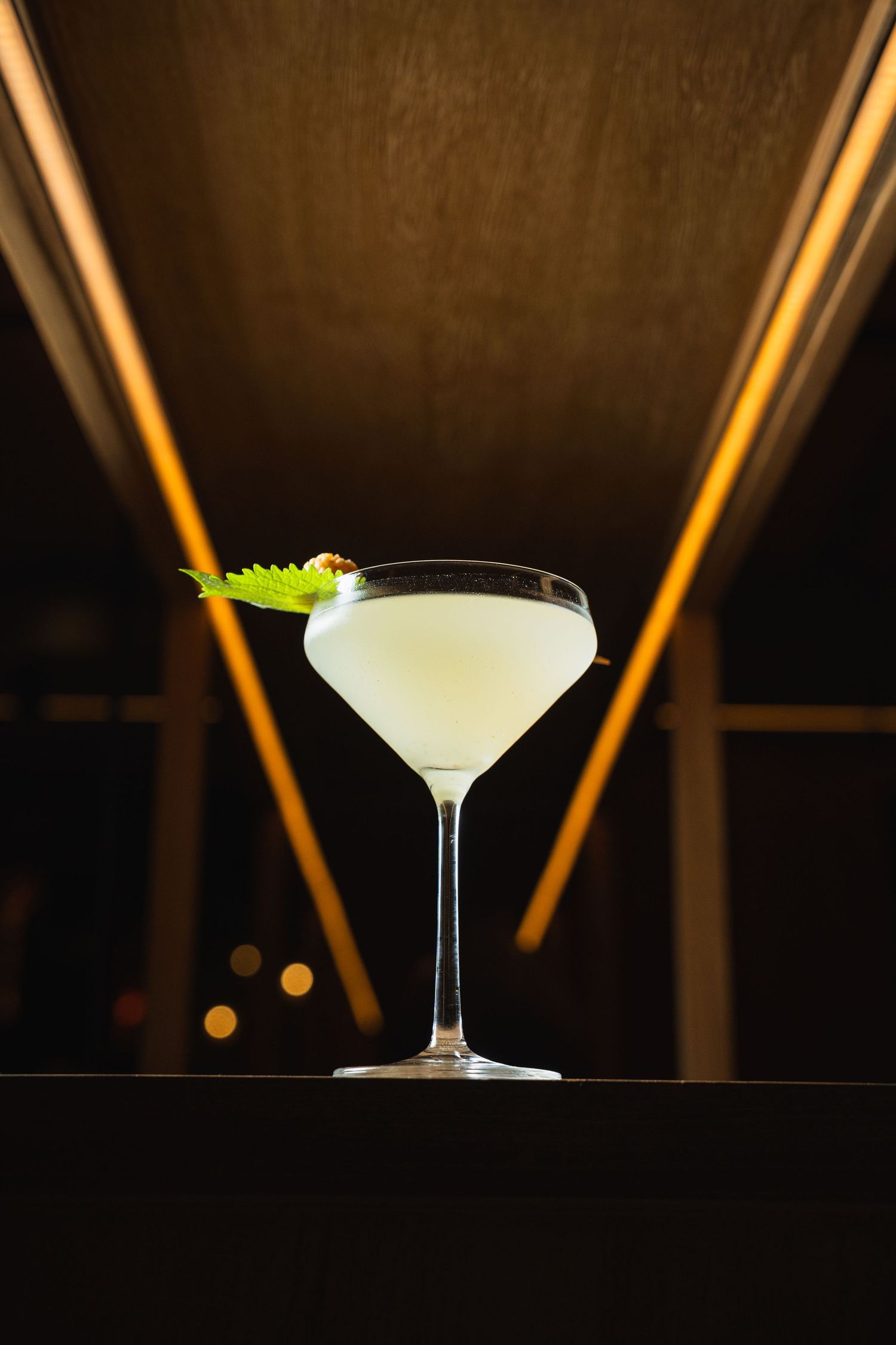 Elegant daiquiri cocktail served in martini glass with lime garnish against dark background with glowing amber lights.