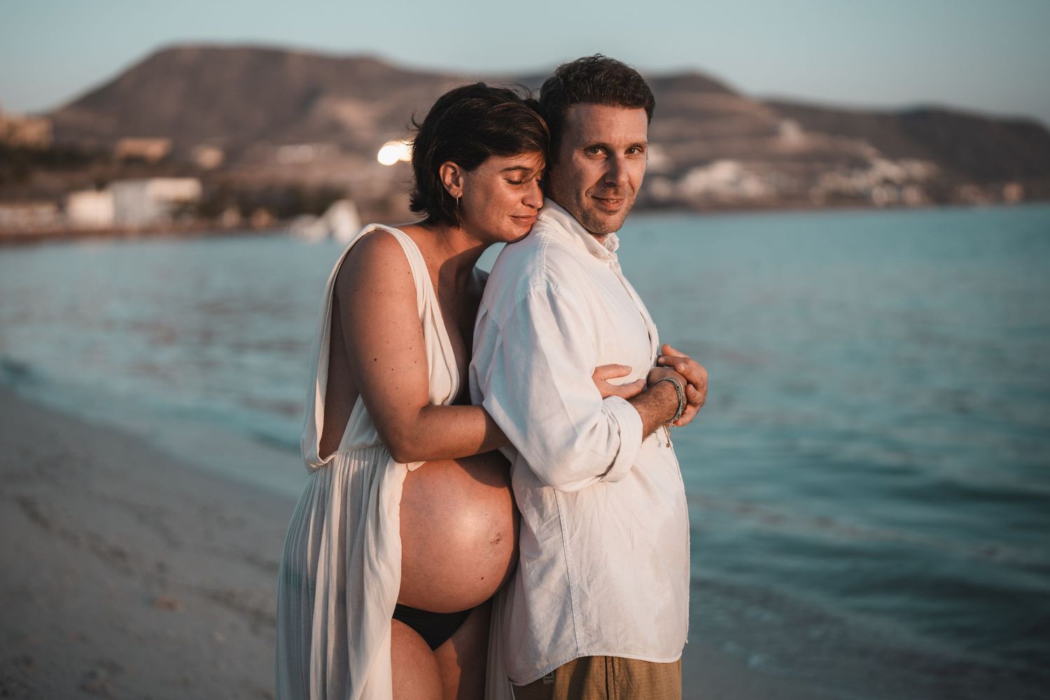 Romantic beachside maternity photoshoot with ocean and mountains in background.