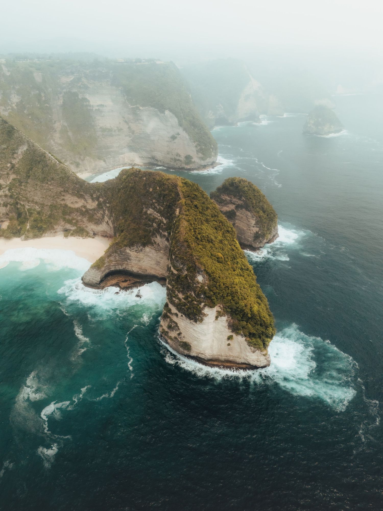 Panoramic view of a misty coastal landscape with dramatic cliffs and turquoise ocean waters.