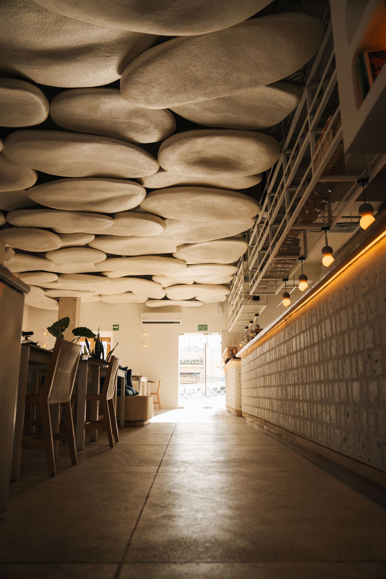 Modern restaurant hallway with sculptural white ceiling panels and dramatic lighting.