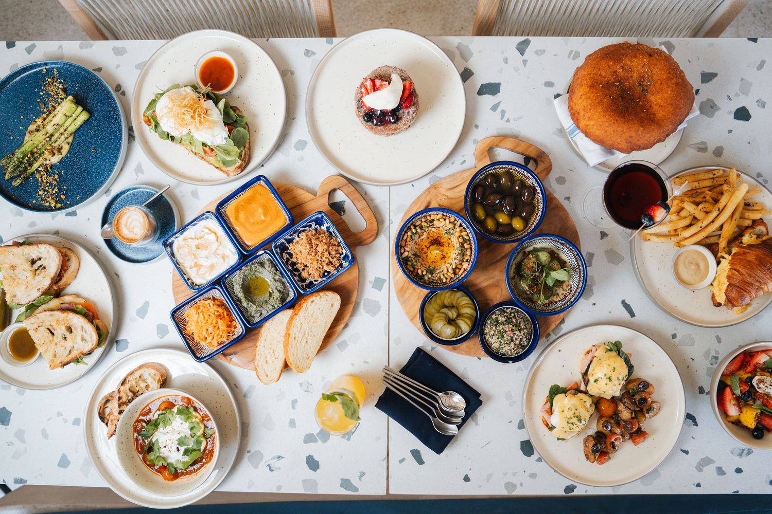 Overhead view of a brunch spread with various dishes including pastries, eggs, salads and sauces on a white marble table.