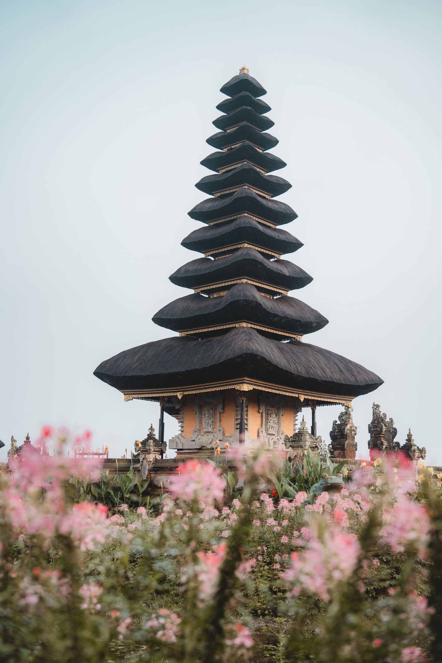 Traditional Balinese temple with multi-tiered pagoda roofs surrounded by pink flowers.