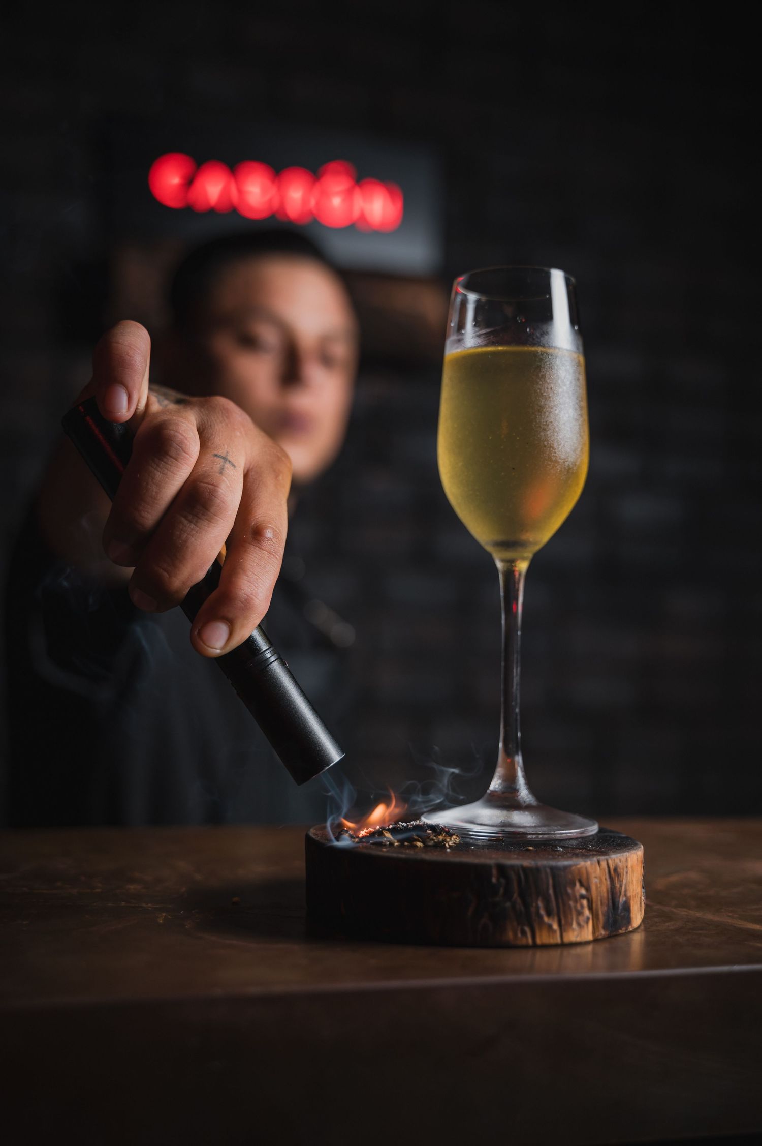 Glass of golden beer being served on a wooden coaster in a dimly lit setting.