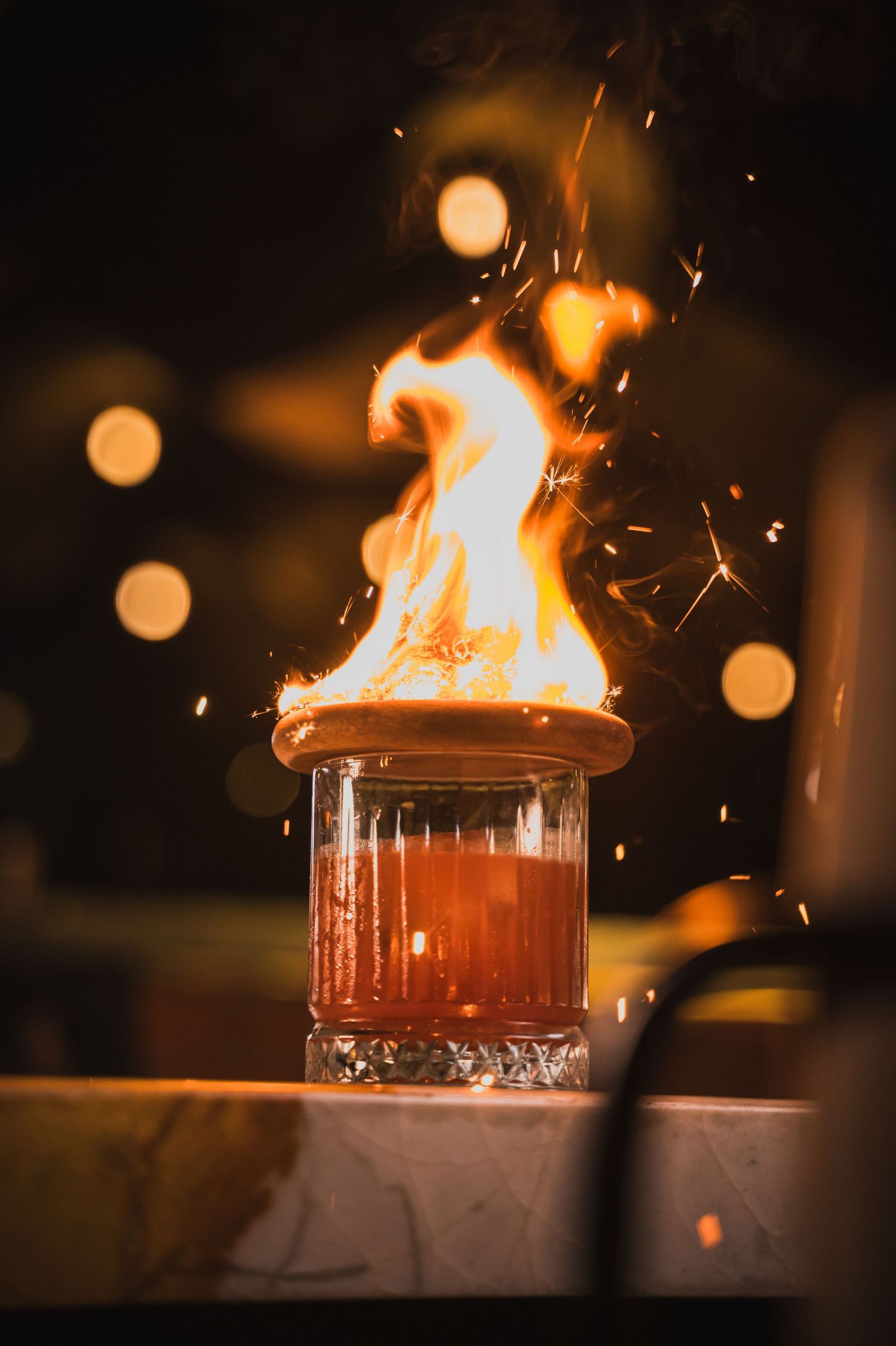 Flaming cocktail in a glass with sparks flying in dramatic nighttime lighting.