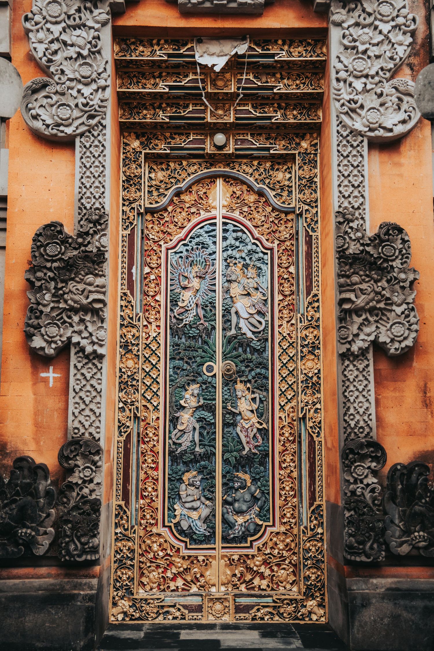 Ornate traditional Balinese temple door with intricate carvings on orange wall.