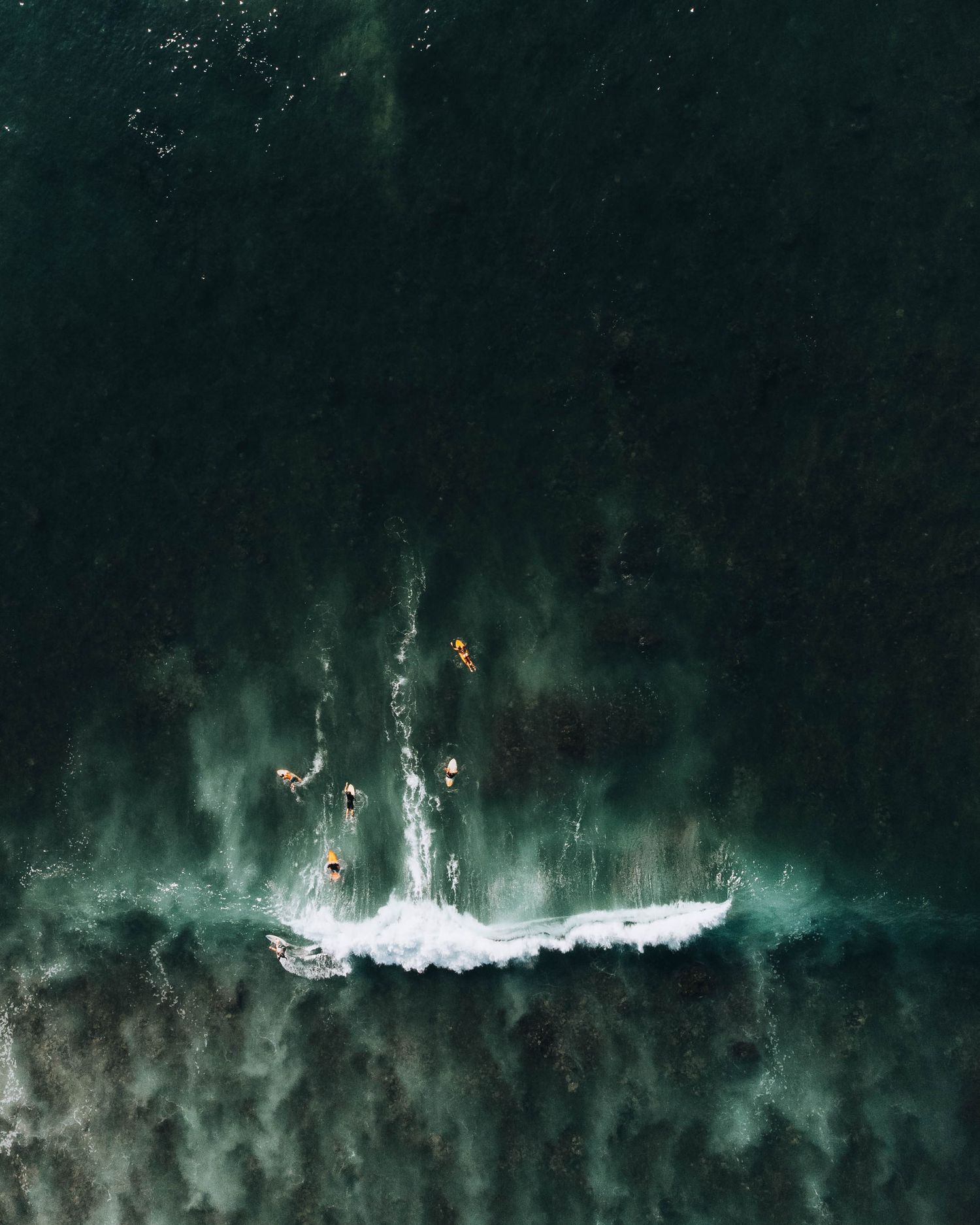 Aerial view of swimmers in dark turquoise waters creating white splashes.