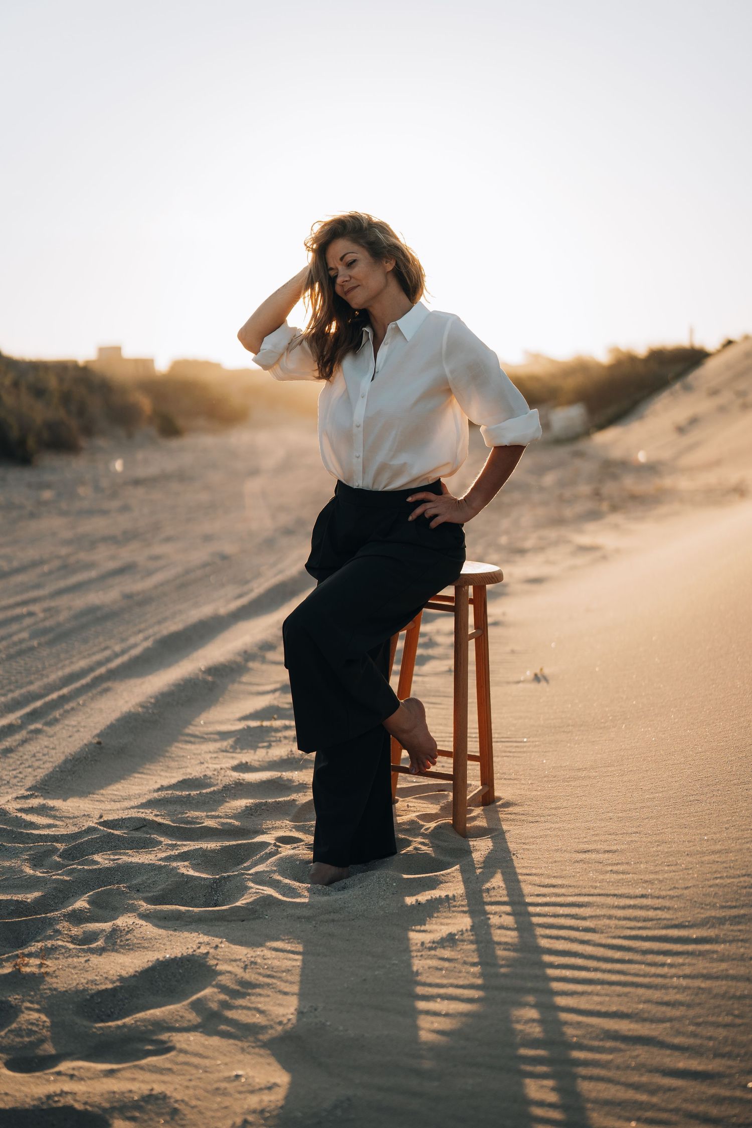 Artistic desert photoshoot with wooden chair and long shadows at sunset.