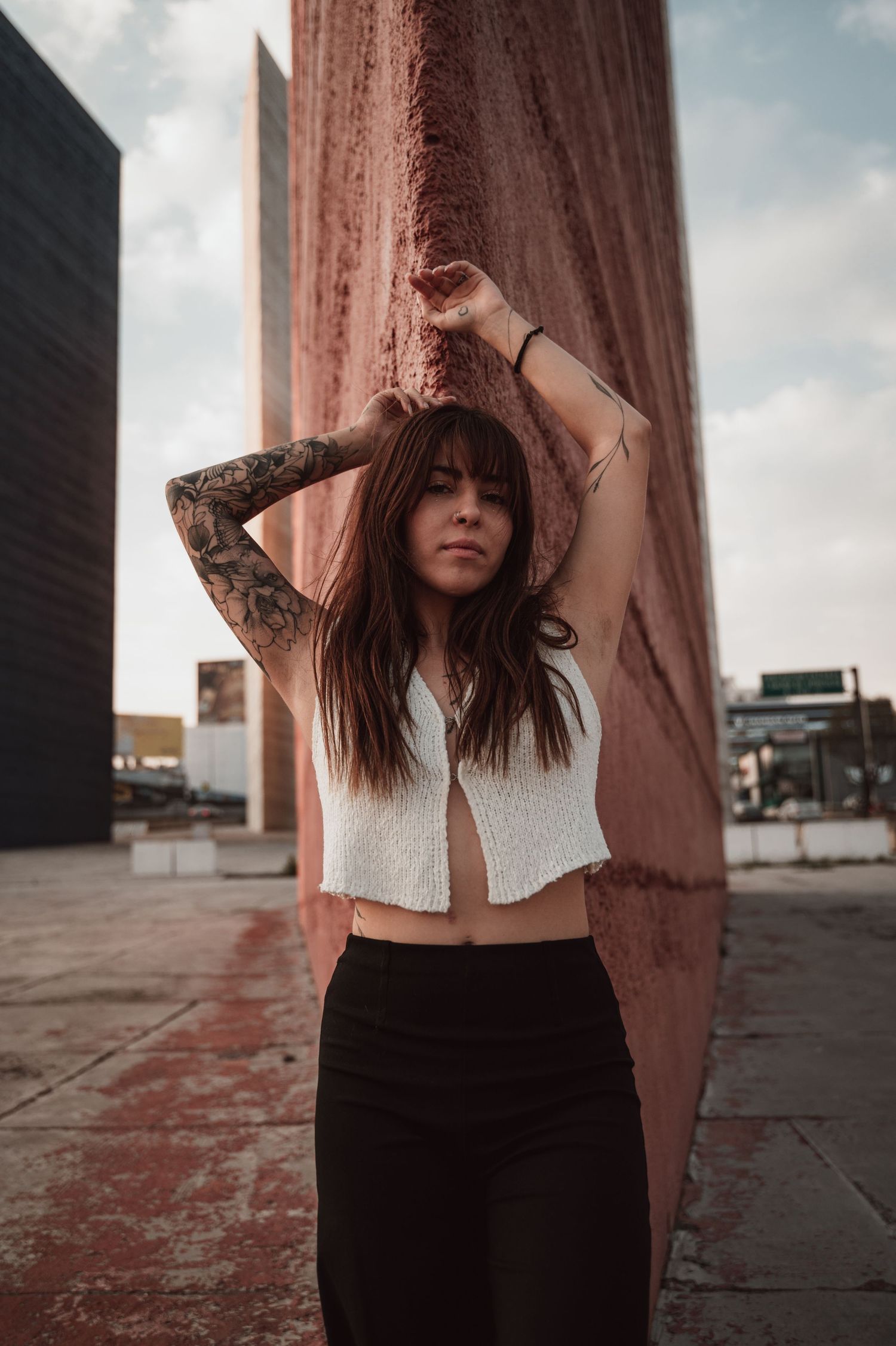 Urban fashion portrait with tattooed arms against a pink wall in casual street style.