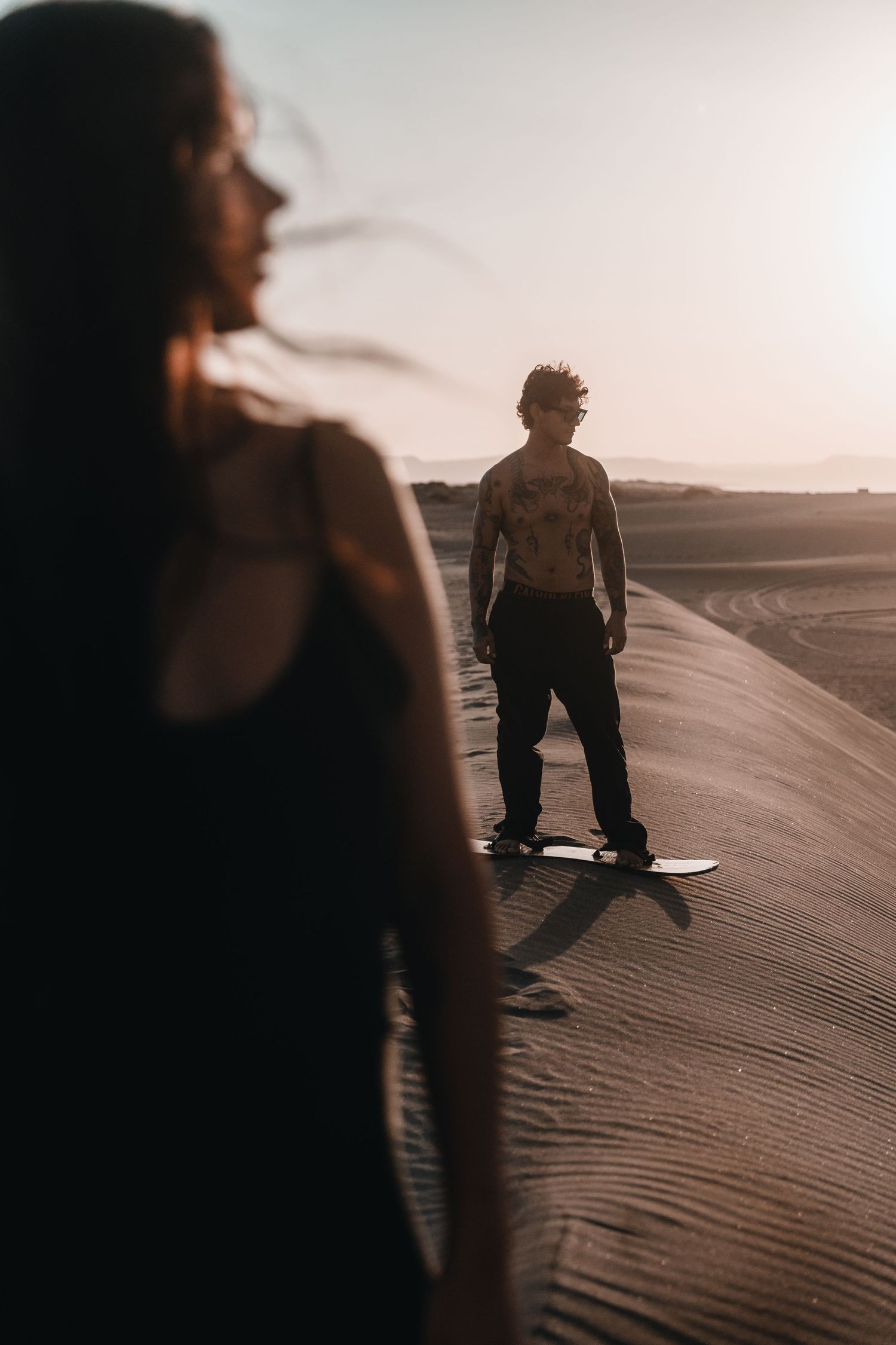Silhouettes walking along sandy desert dunes at sunset with long shadows cast across rippled sand.