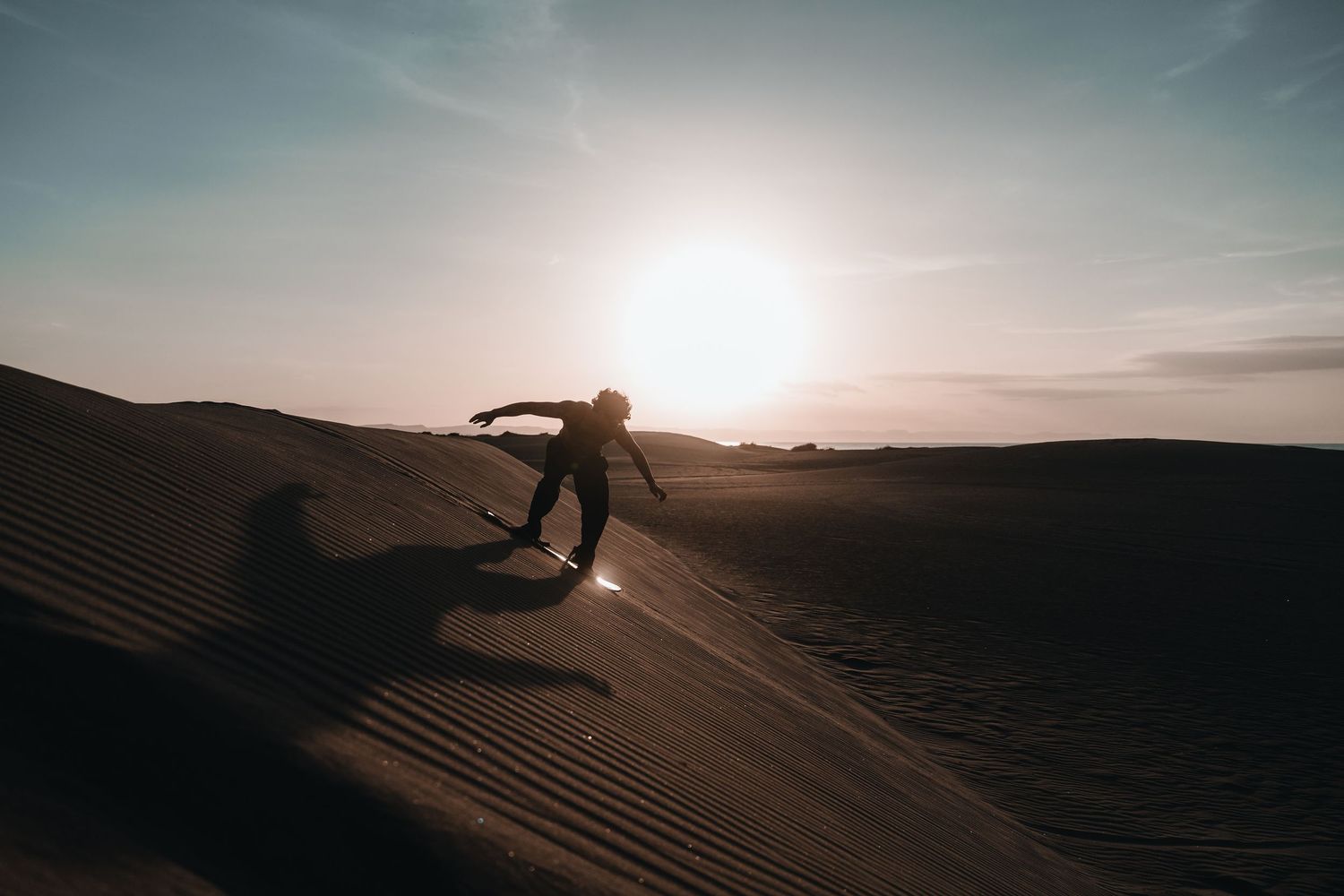 Desert landscape photographed at sunset showing sweeping sand dunes and dramatic sky.