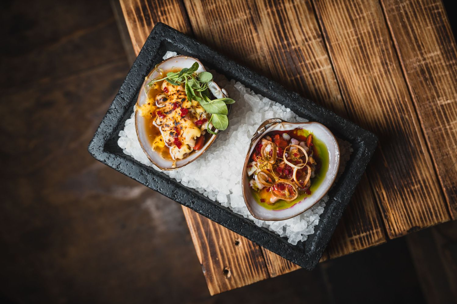 Close-up shot of modern gourmet dishes plated on dark stone surfaces in a rustic wooden setting.