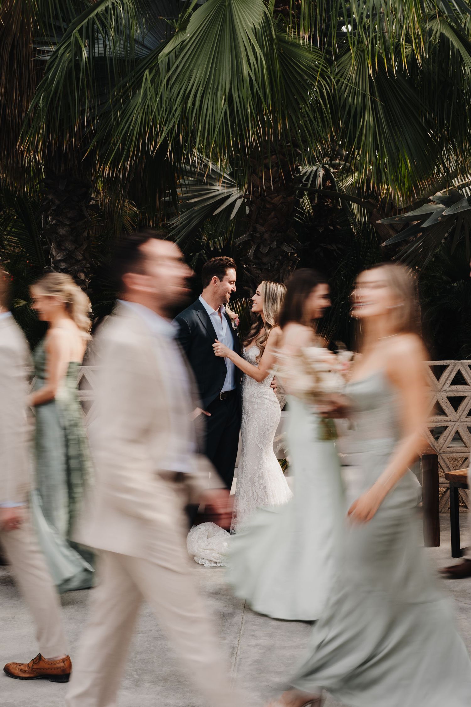 Motion blur capture of wedding party walking past tropical foliage.