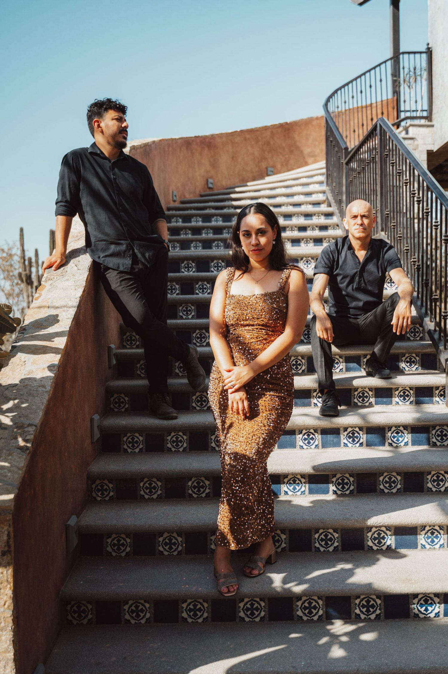 Three people posed on decorative tiled steps against a rustic architectural backdrop.
