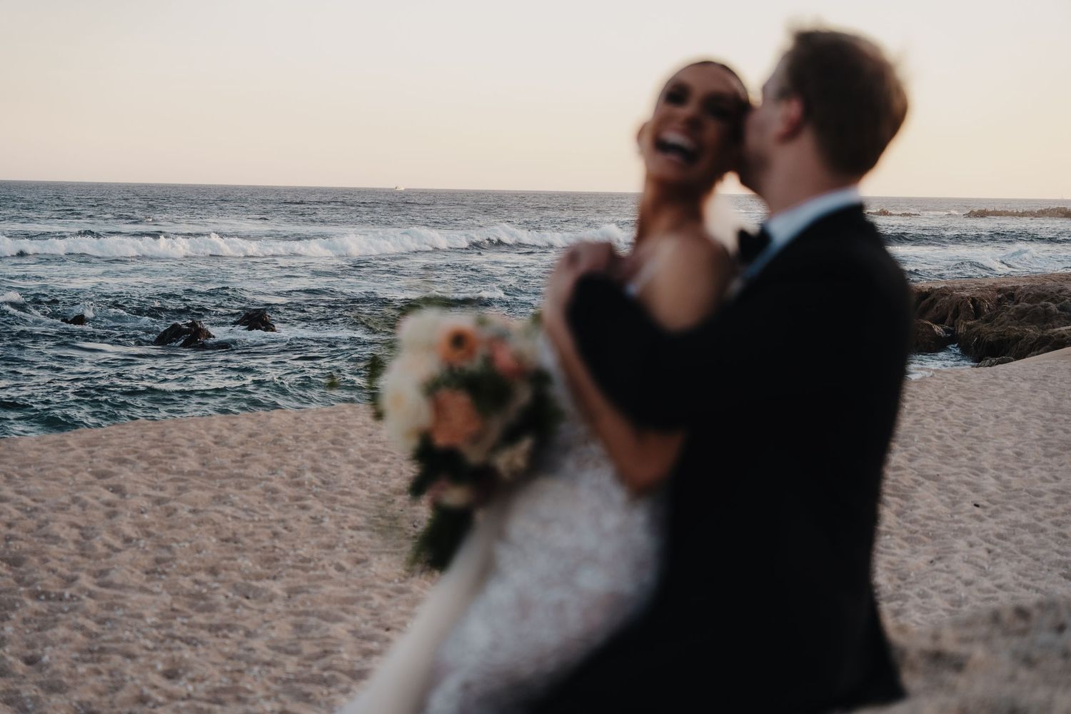 A romantic moment between newlyweds on a sandy beach with ocean waves in the background.