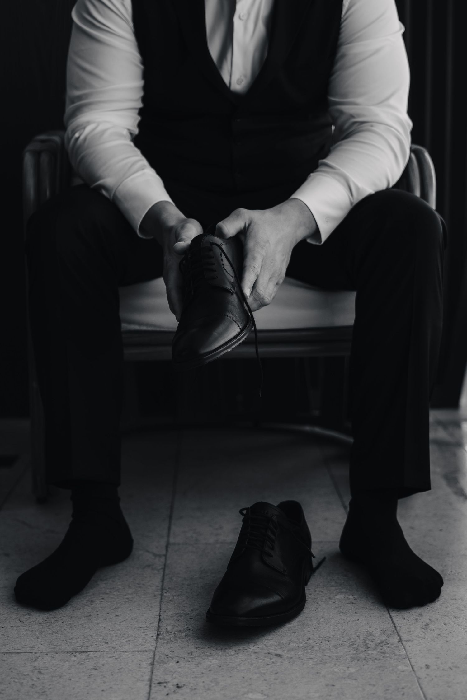 Close-up shot of a groom in formal attire putting on black dress shoes.