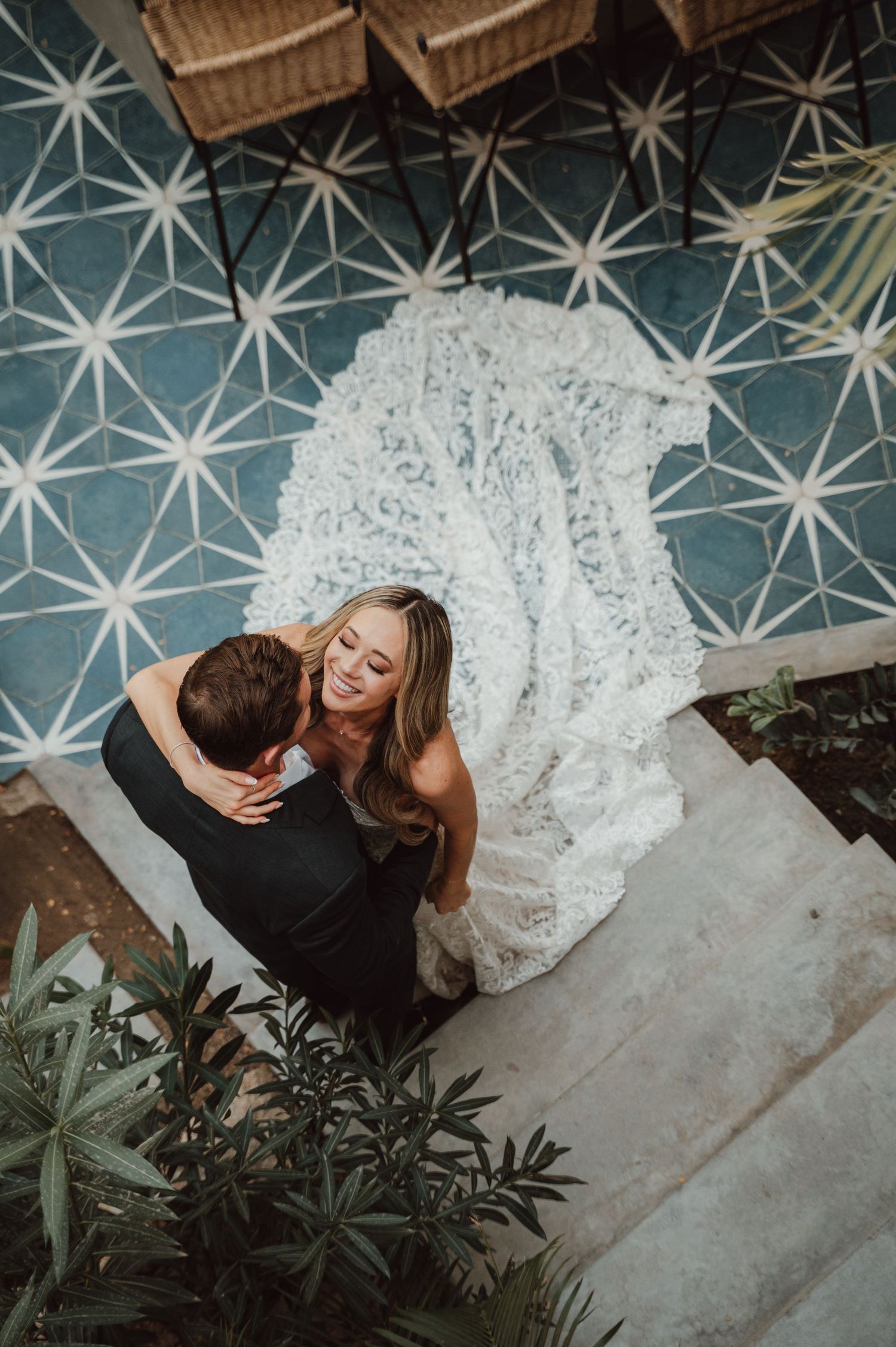 Overhead view of couple embracing on geometric tiled floor with wicker furniture visible.