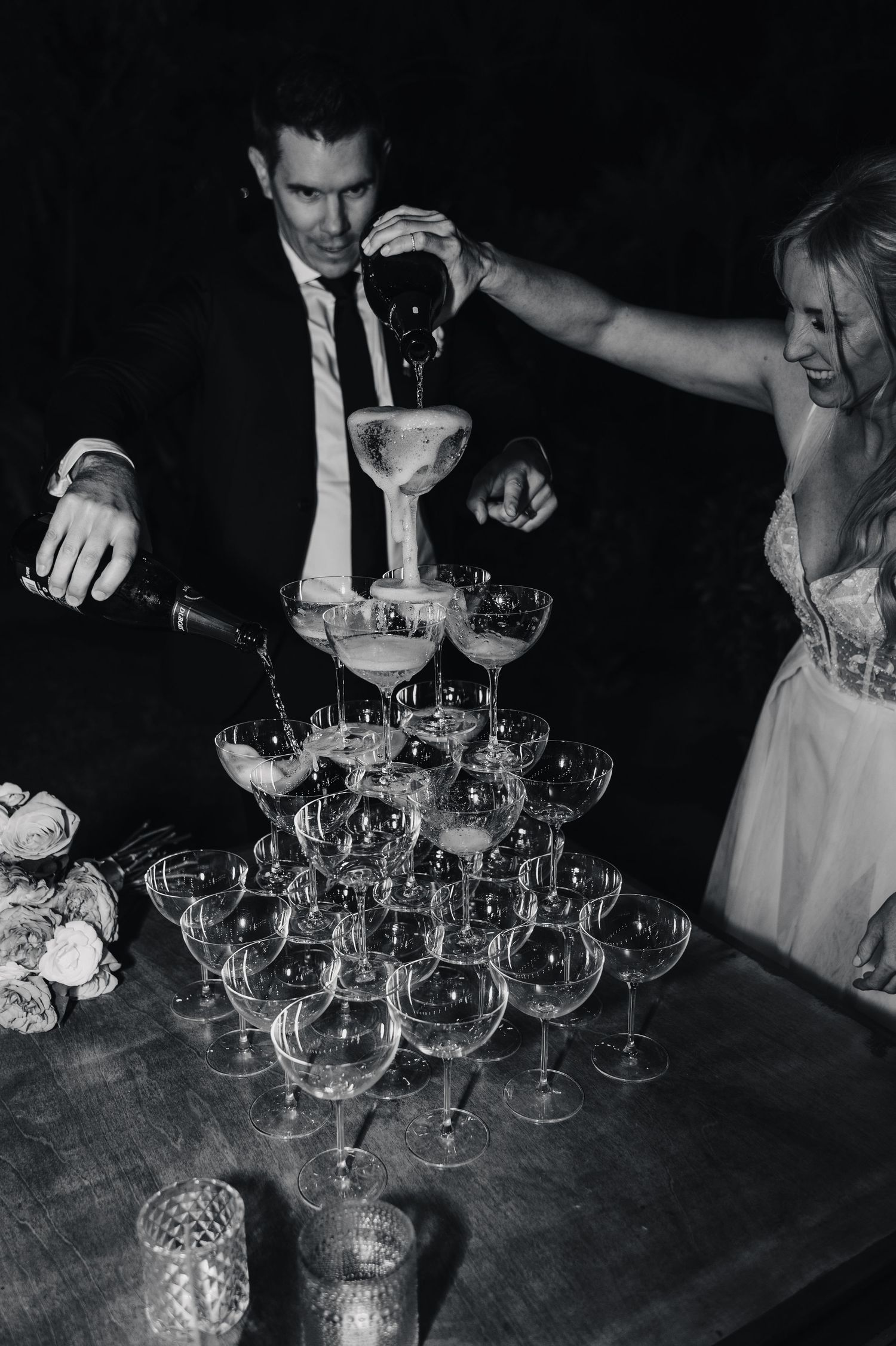 Black and white photo of champagne glasses being arranged on a wooden table.